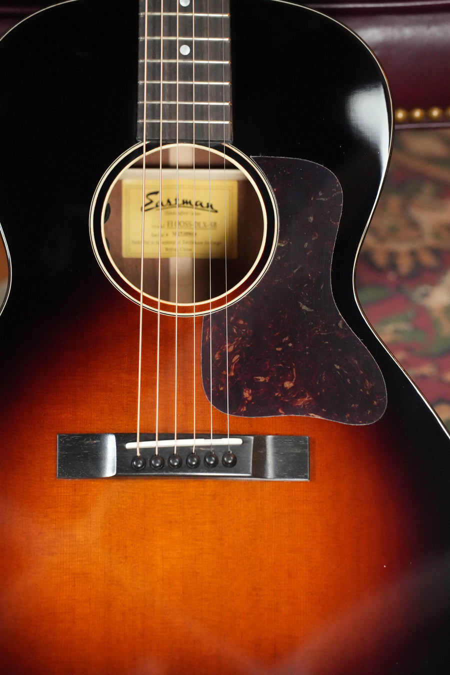 A close-up of the Eastman Guitars E1OOSS-DLX-SB Sunburst 00 Acoustic-Electric Guitar #8804 highlights its strings, sound hole label, tortoiseshell-style pickguard, and fretboard, capturing a classic pre-war vibe.