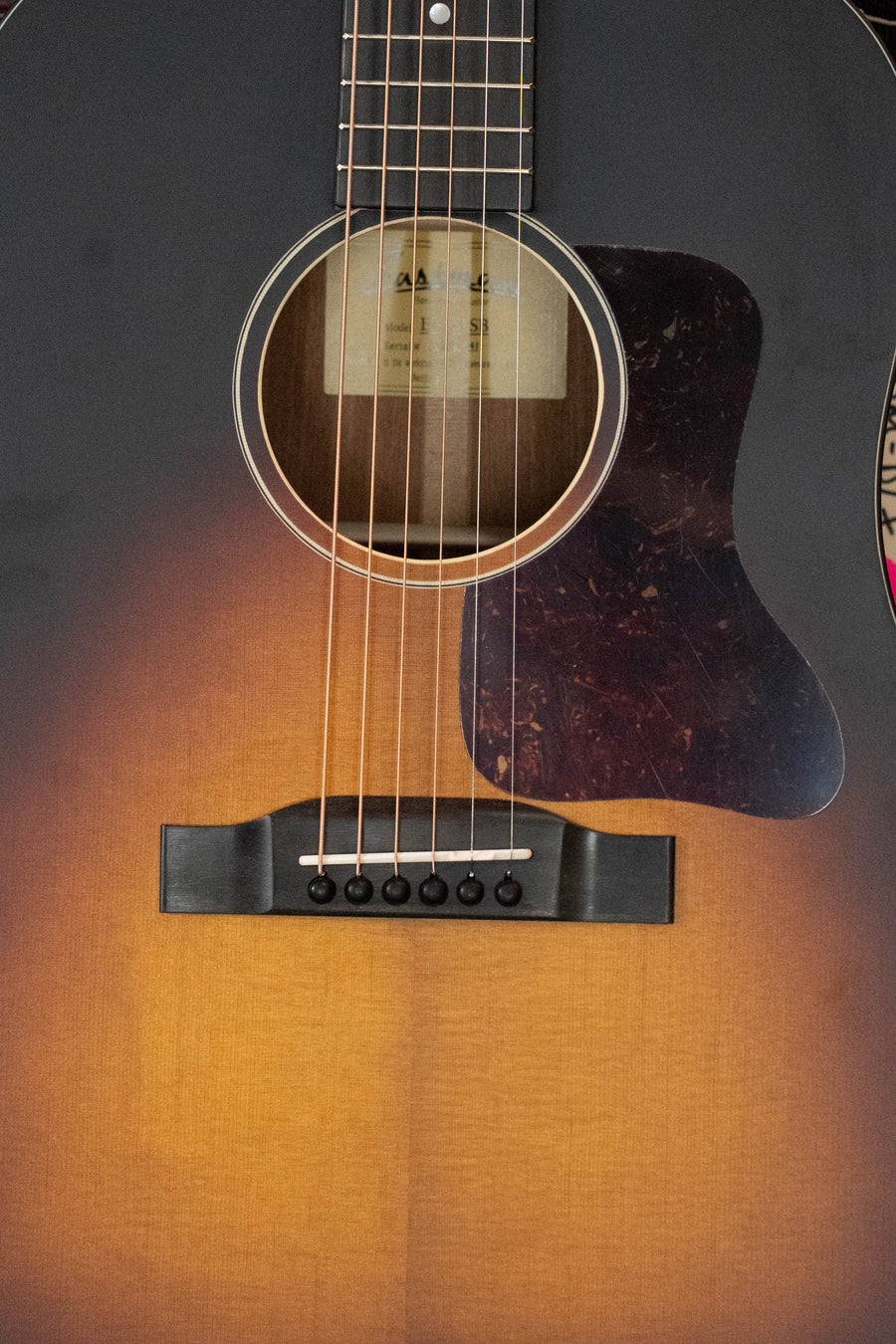 Close-up of the Eastman Guitars E1SS-SB Sitka/Sapele Sunburst Slope Shoulder Dreadnought Acoustic Guitar #1441, showing its sunburst finish, dark pickguard, six strings, bridge, and soundhole.