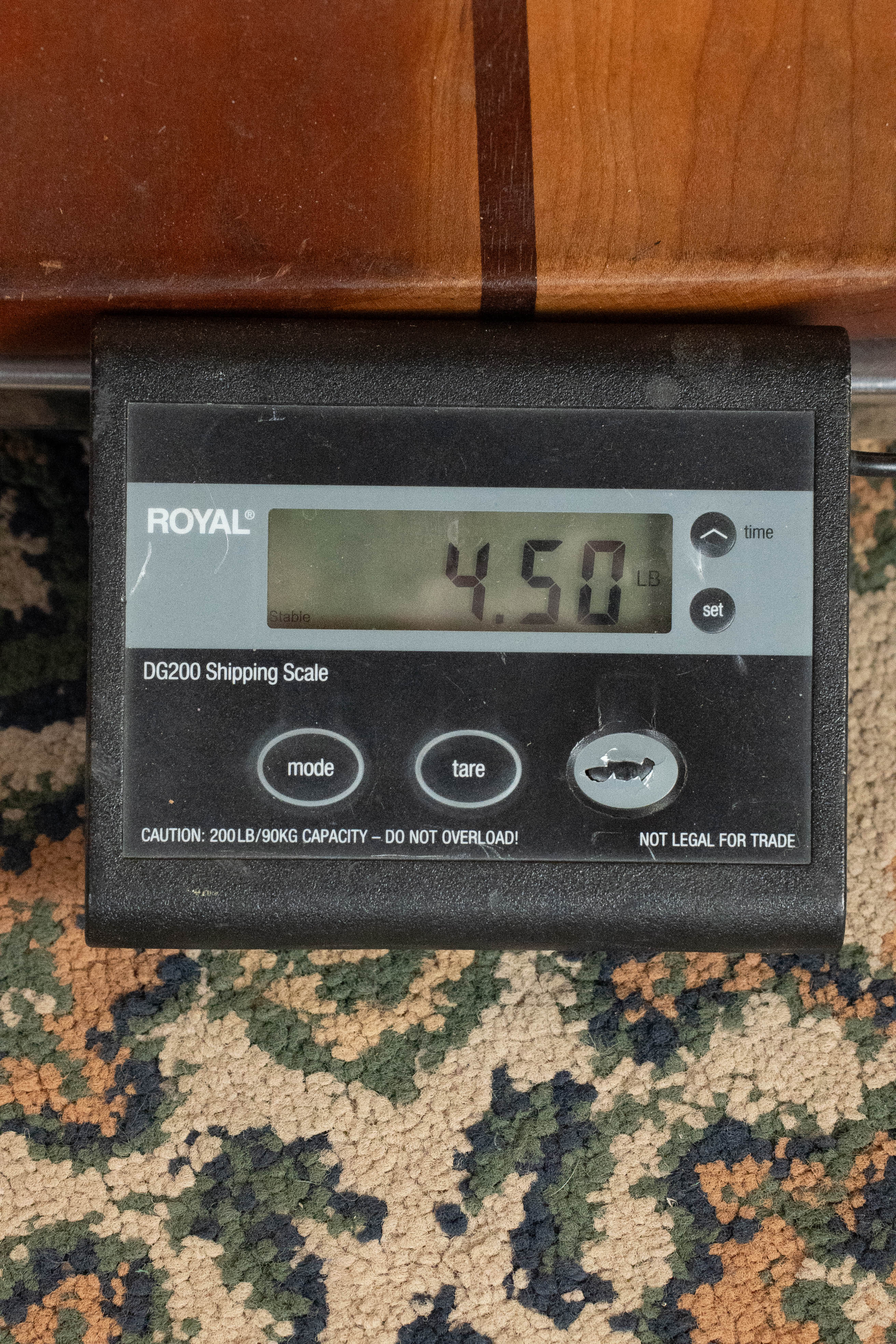 A digital shipping scale on a patterned carpet shows 4.50 lbs, ideal for weighing items like the Eastman Guitars E20D-LSH-TC Thermo-Cured Adirondack/Rosewood Large Soundhole Dreadnought Acoustic Guitar #3917.