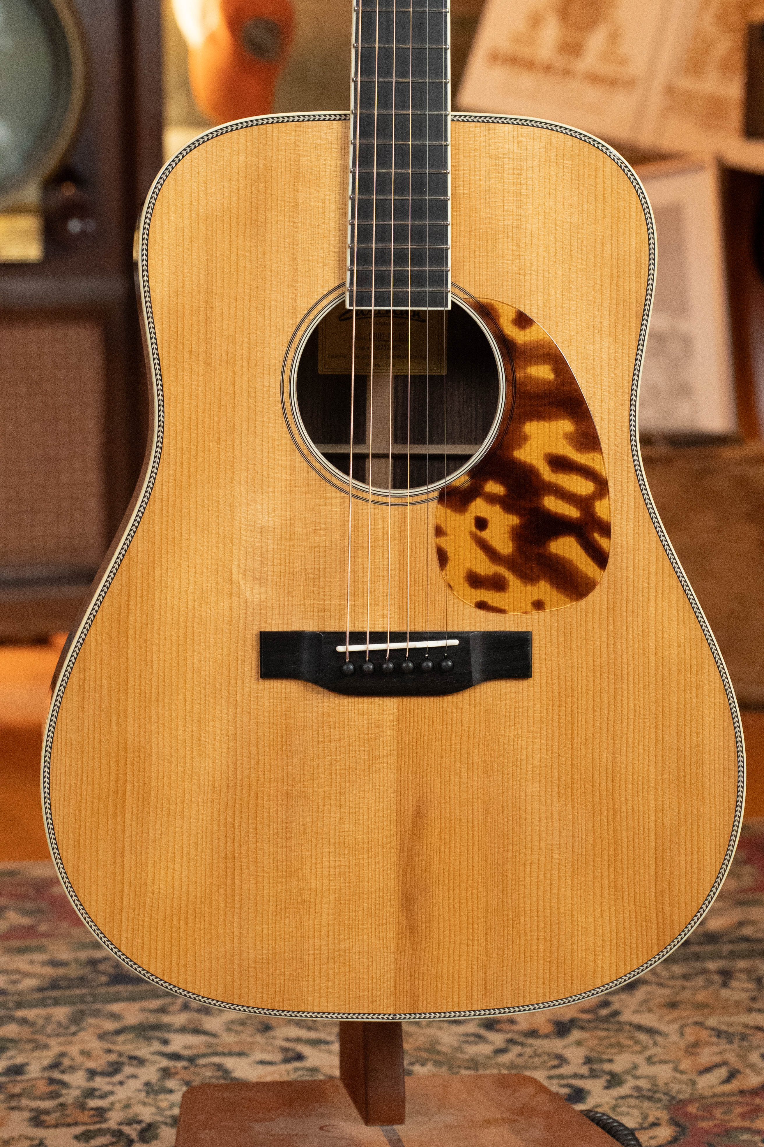A close-up of an Eastman Guitars E20D-LSH-TC #3917 dreadnought acoustic guitar with a thermo-cured Adirondack Spruce top and rosewood body, large soundhole, tortoiseshell pickguard, and detailed binding, resting on a stand in warm light.