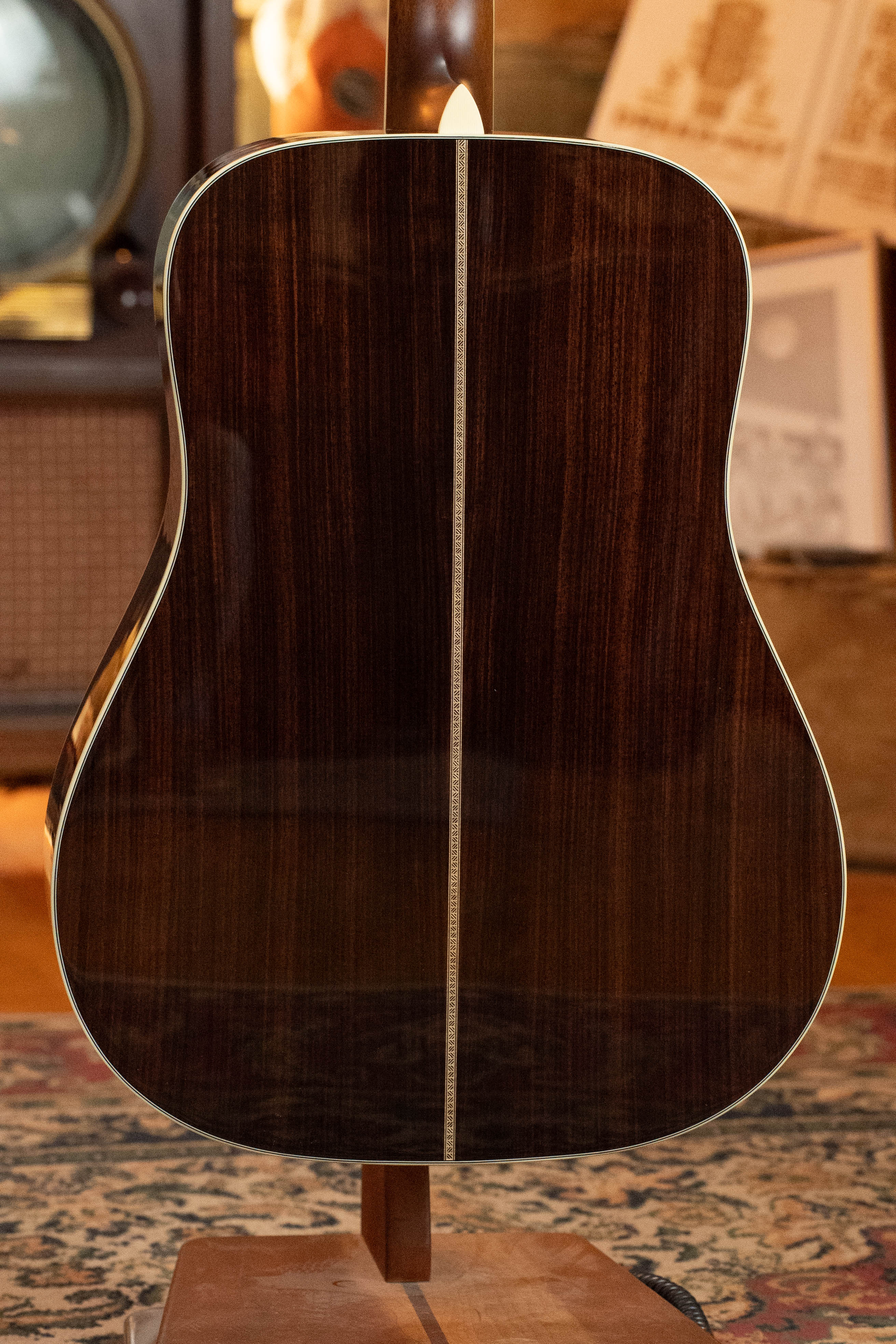The image shows the back of an Eastman Guitars E20D-LSH-TC Thermo-Cured Adirondack/Rosewood Large Soundhole Dreadnought Acoustic Guitar #8072, with a rich wood finish and center strip, on a stand in a vintage-themed room with sheet music.