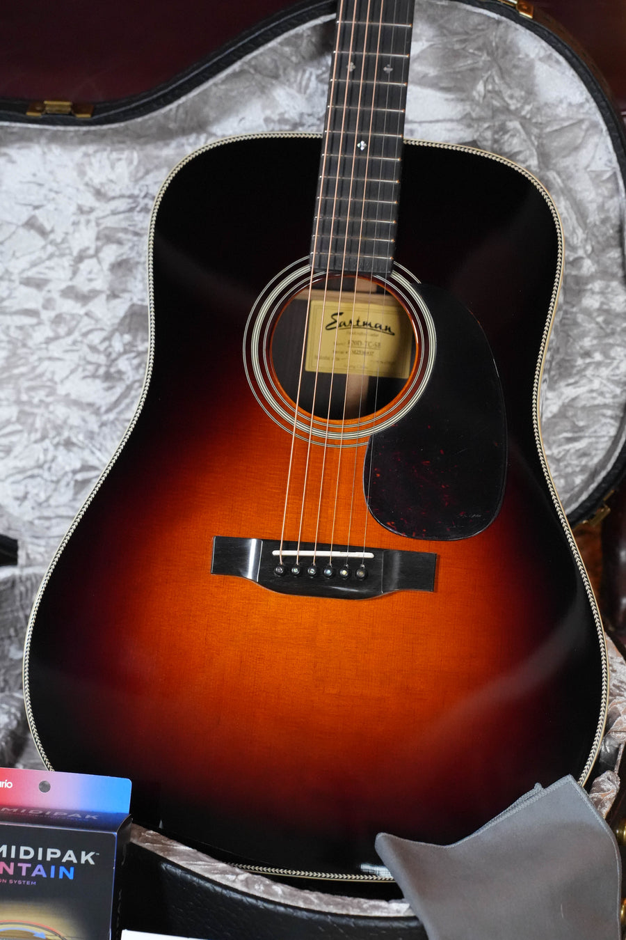 An Eastman Guitars E20D-TC-SB Thermo-Cured Adirondack/Rosewood Dreadnought Acoustic Guitar #6437 with sunburst finish and black pickguard rests in an open, plush-lined hard case, with a cleaning cloth and Humidipak pack included.