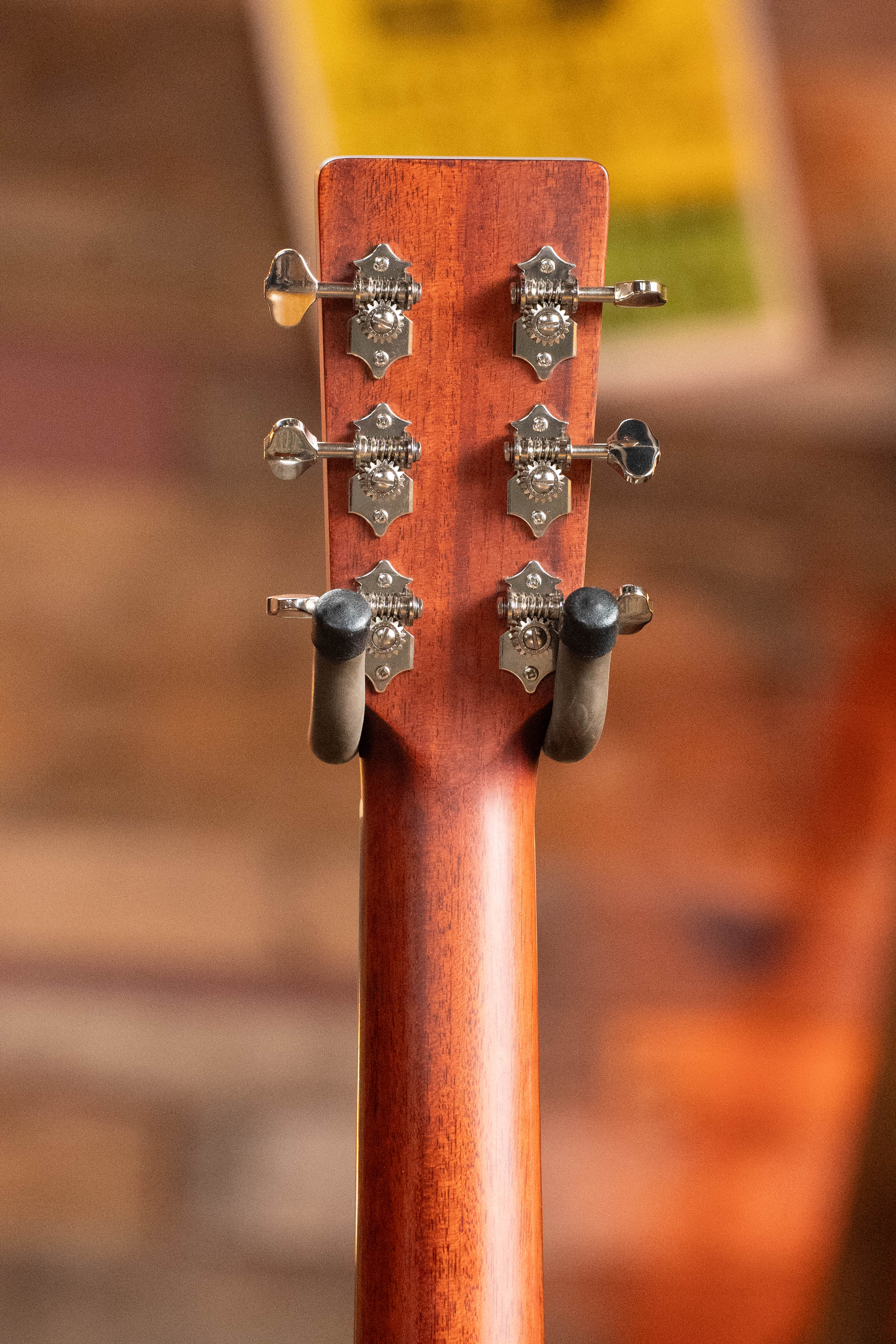 Close-up of the back of an Eastman Guitars E2D-DLX-SB Cedar/Sapele Sunburst Dreadnought (#1532) headstock, showing six metal tuners and black stand arms, with a warm-toned blurred background.