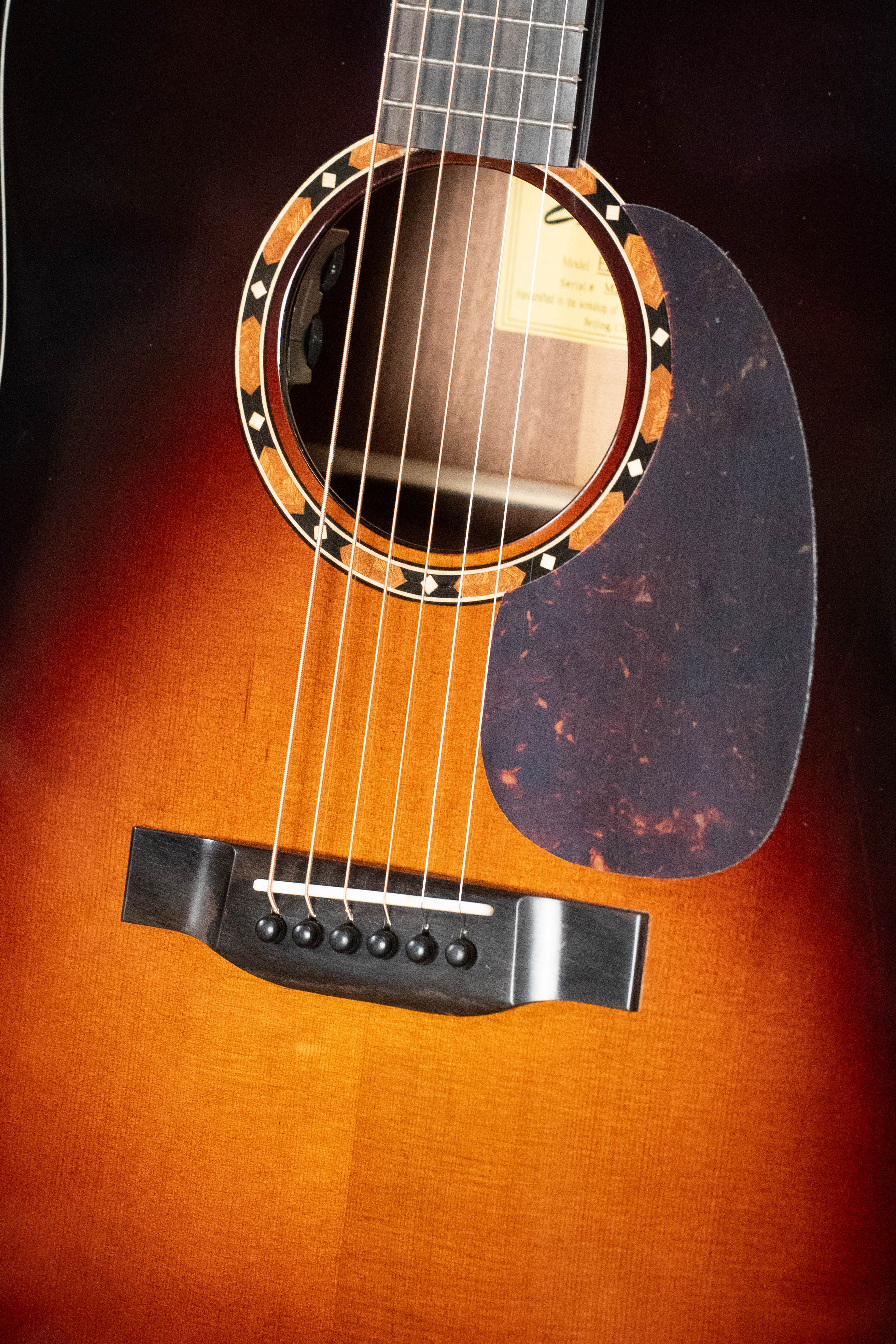Close-up of an Eastman Guitars E2D-DLX-SB Cedar/Sapele Sunburst Dreadnought (#1532), highlighting the strings, decorative soundhole inlay, black pickguard, bridge with six black pins, and Fishman pickup.