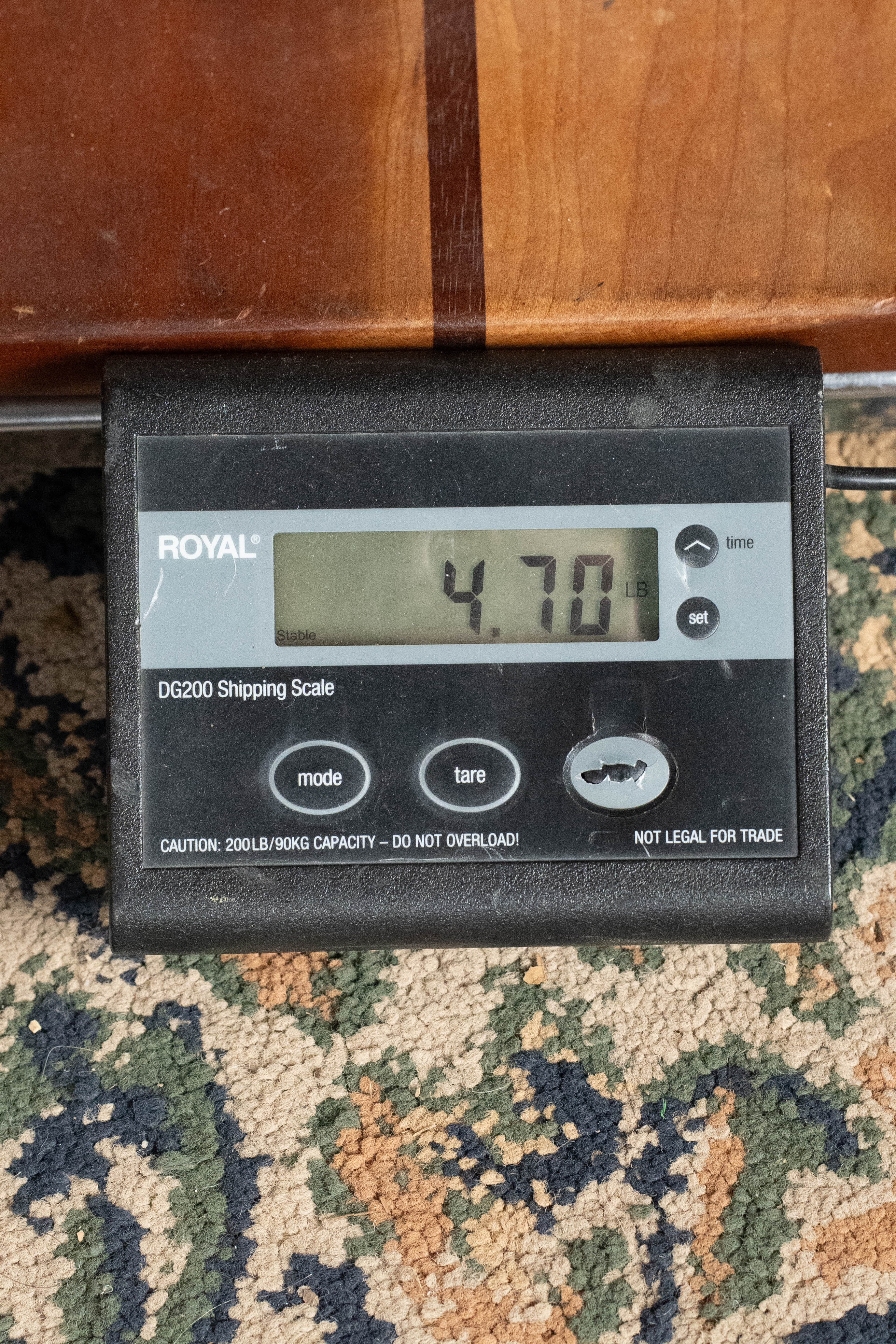 A digital shipping scale reads 4.70 pounds. Nearby rests an Eastman Guitars E2D-DLX-SB Cedar/Sapele Sunburst Dreadnought Guitar with Fishman Pickup #1532, partly under a wooden surface on patterned carpet.