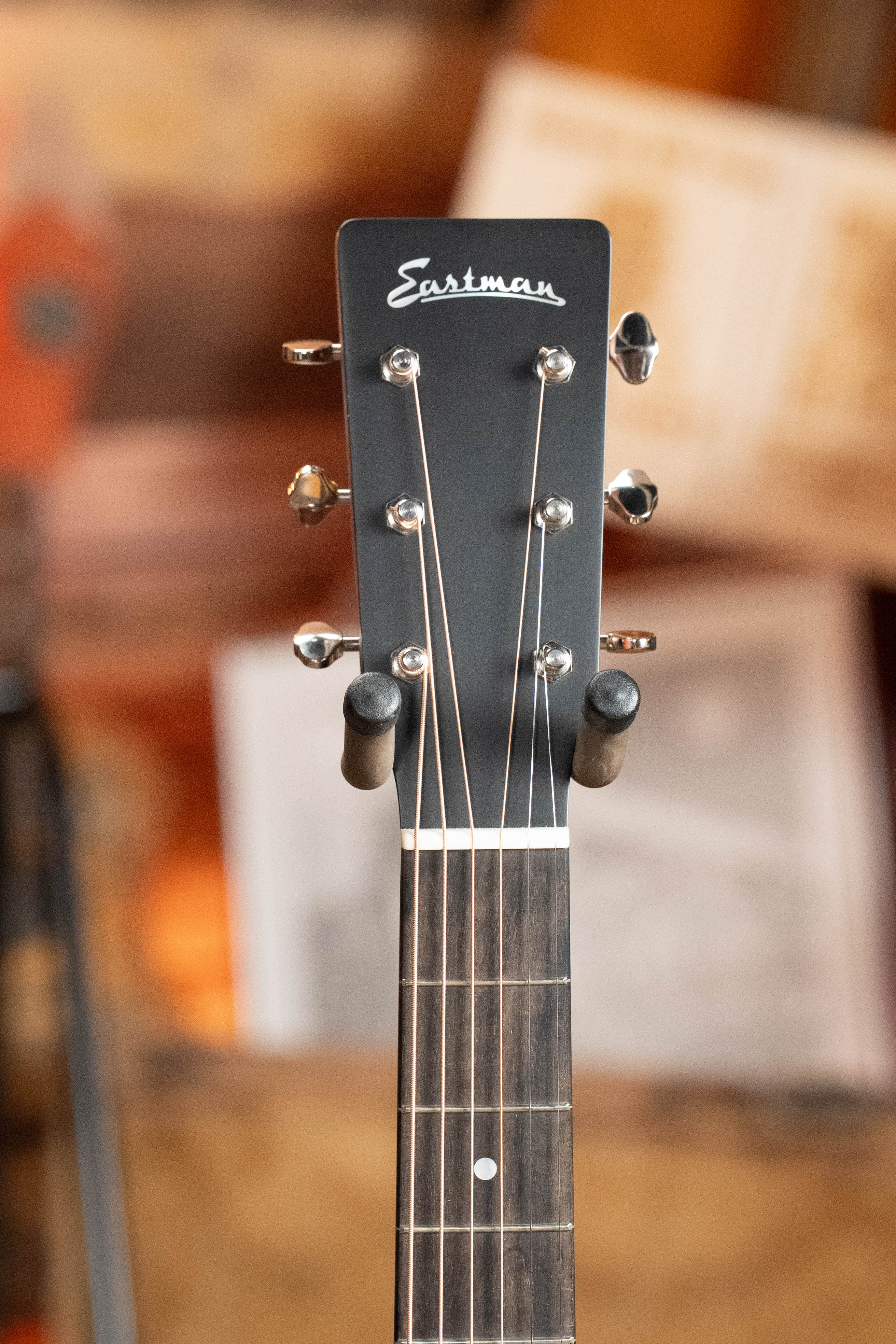 Close-up of an Eastman Guitars E2D-DLX-SB Cedar/Sapele Sunburst Dreadnought Guitar w/Fishman Pickup #1532 headstock, showing six tuning pegs and part of the fretboard against a warm, softly blurred brown and orange background.