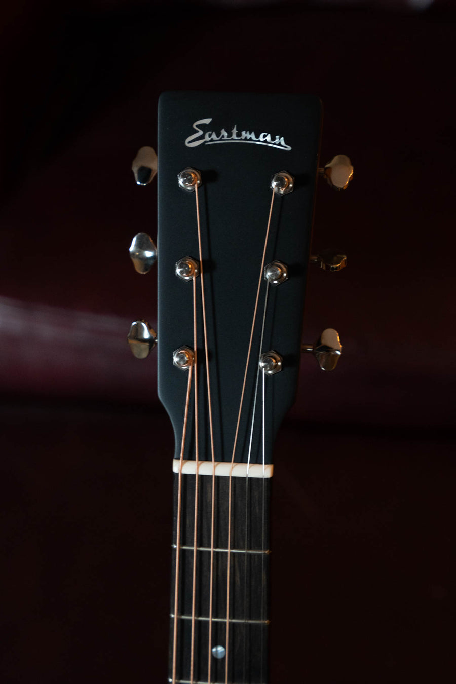 Close-up of the headstock of an Eastman Guitars E2OM-DLX-SB Cedar/Sapele Sunburst Orchestra Model Guitar w/Fishman Pickup #4173, showing tuning pegs, strings, and the Eastman logo against a dark background.
