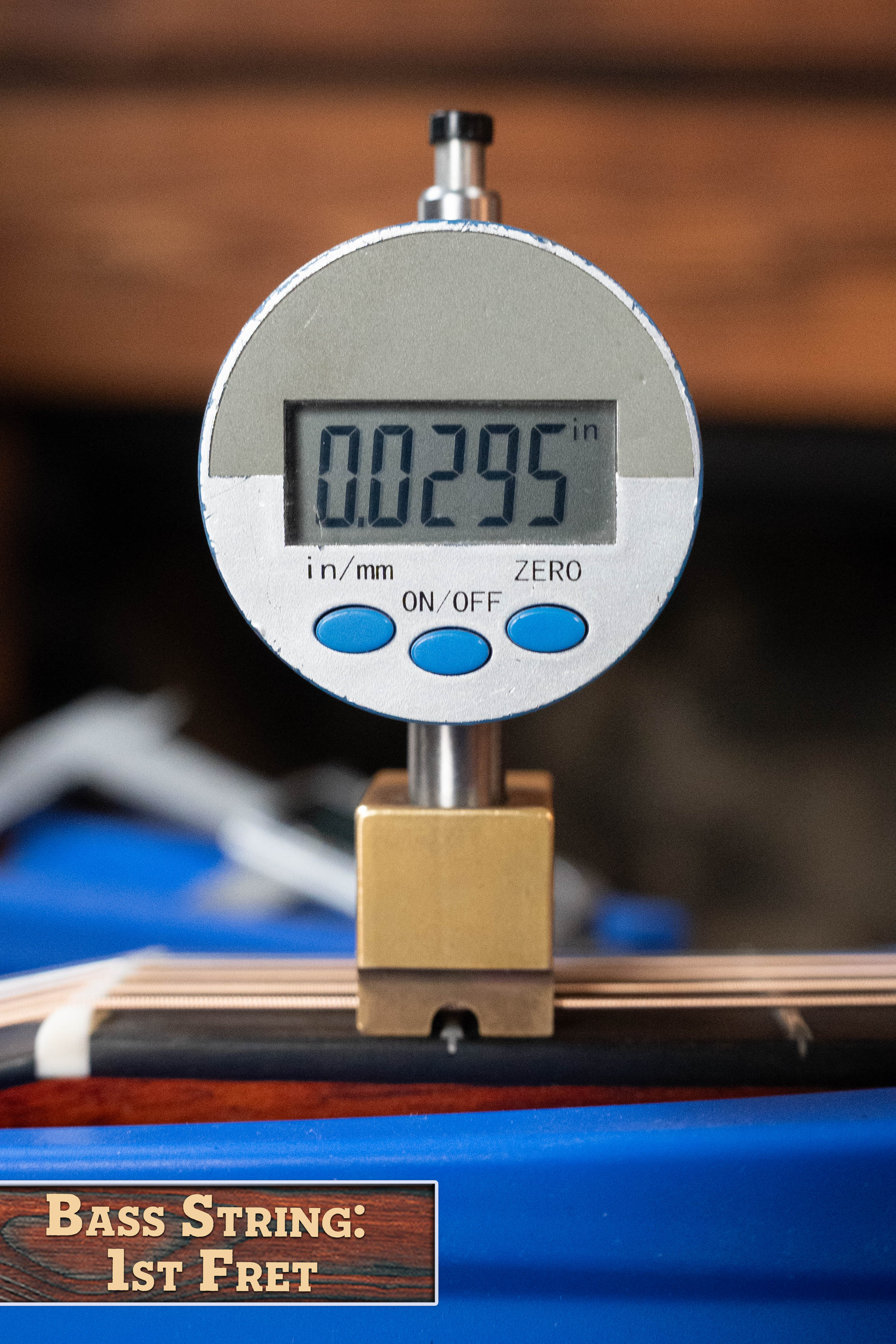 A digital gauge shows 0.0295 inches, measuring the string height at the 1st fret of an Eastman E2OM Cedar/Sapele Orchestra Model Acoustic Guitar (#9002) by Eastman Guitars. A sign reads: Bass String: 1st Fret.