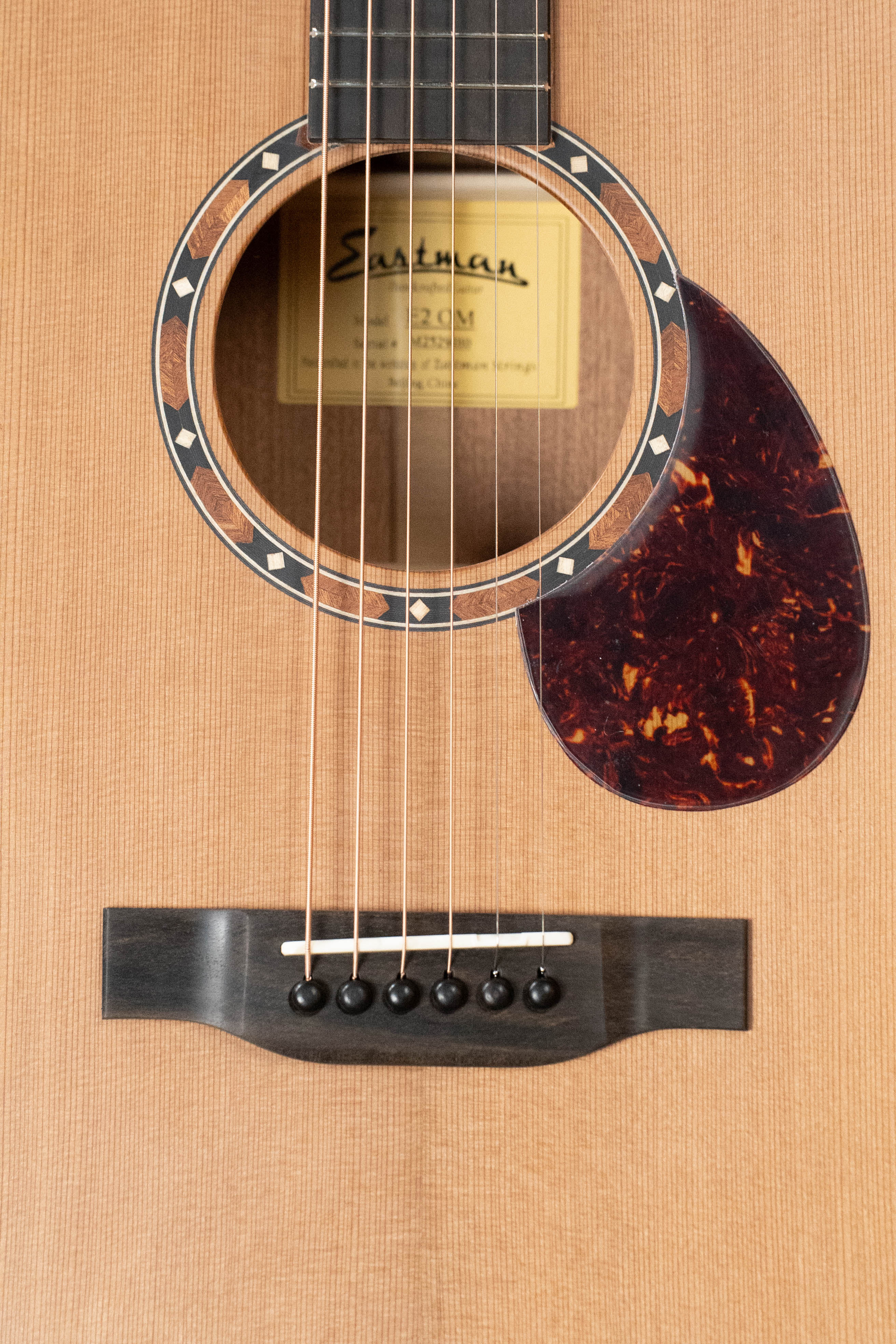 Close-up of an Eastman Guitars E2OM Cedar/Sapele Orchestra Model Acoustic Guitar #9010’s body, highlighting the soundhole, pickguard, bridge, strings, and interior label—a superb option for fingerstyle players.