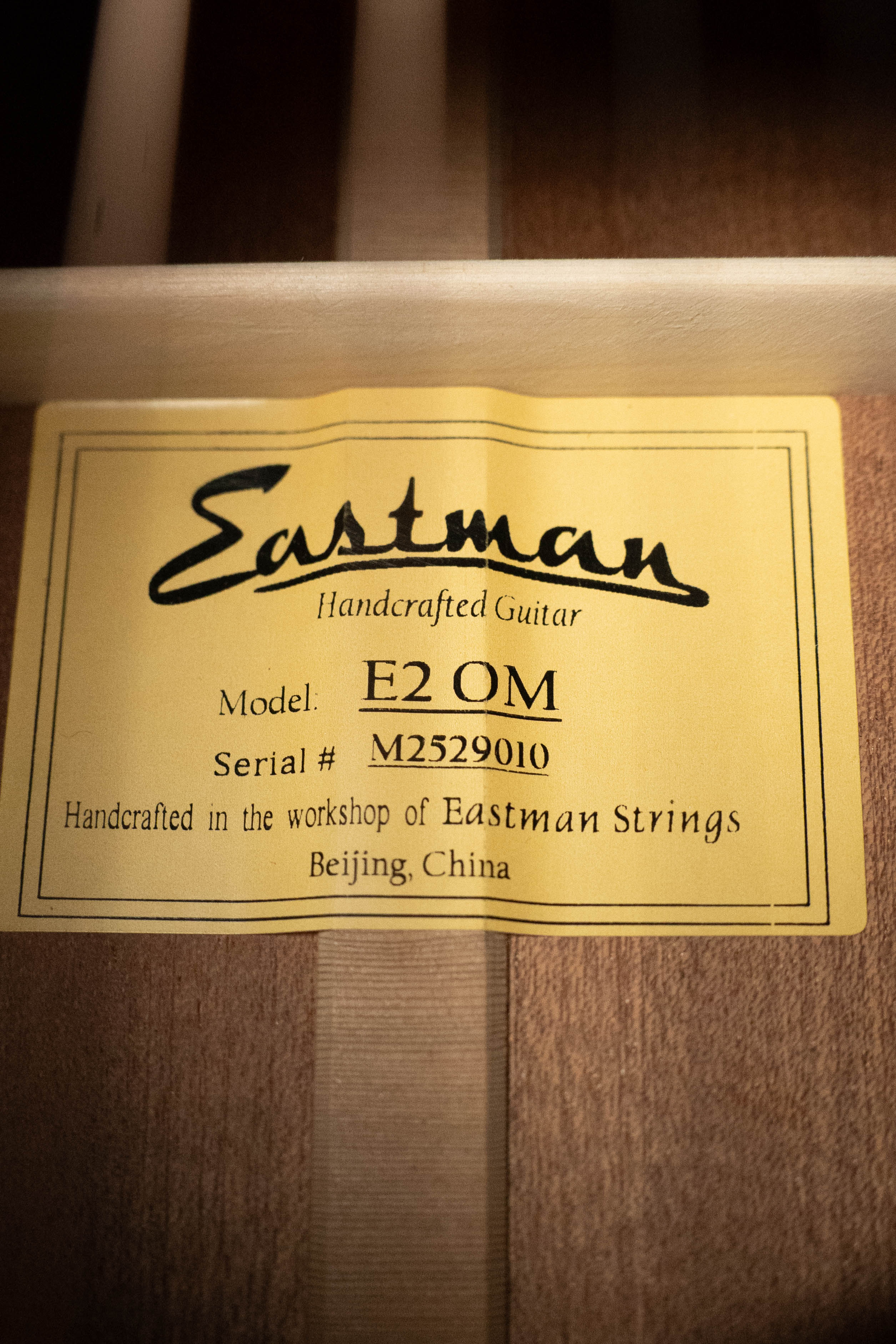 A yellow label inside the guitar reads: Eastman Guitars E2OM Cedar/Sapele Orchestra Model Acoustic Guitar #9010. Handcrafted in Beijing, China, it's perfect for fingerstyle playing.