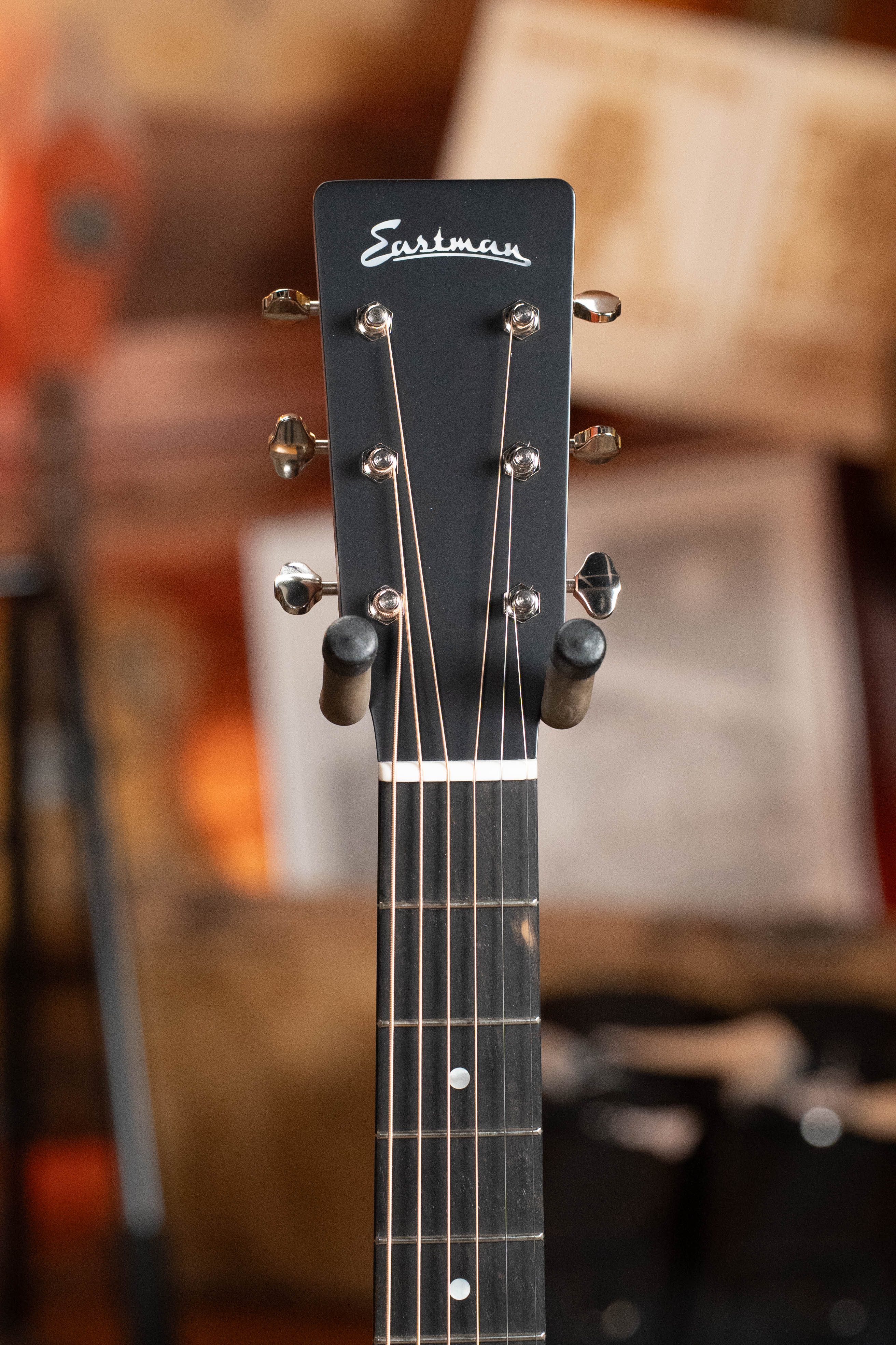 Close-up of the headstock of an Eastman Guitars E2OM Cedar/Sapele Orchestra Model Acoustic Guitar #9010, highlighting tuning pegs and strings against a warm, blurred background—ideal for fingerstyle enthusiasts.