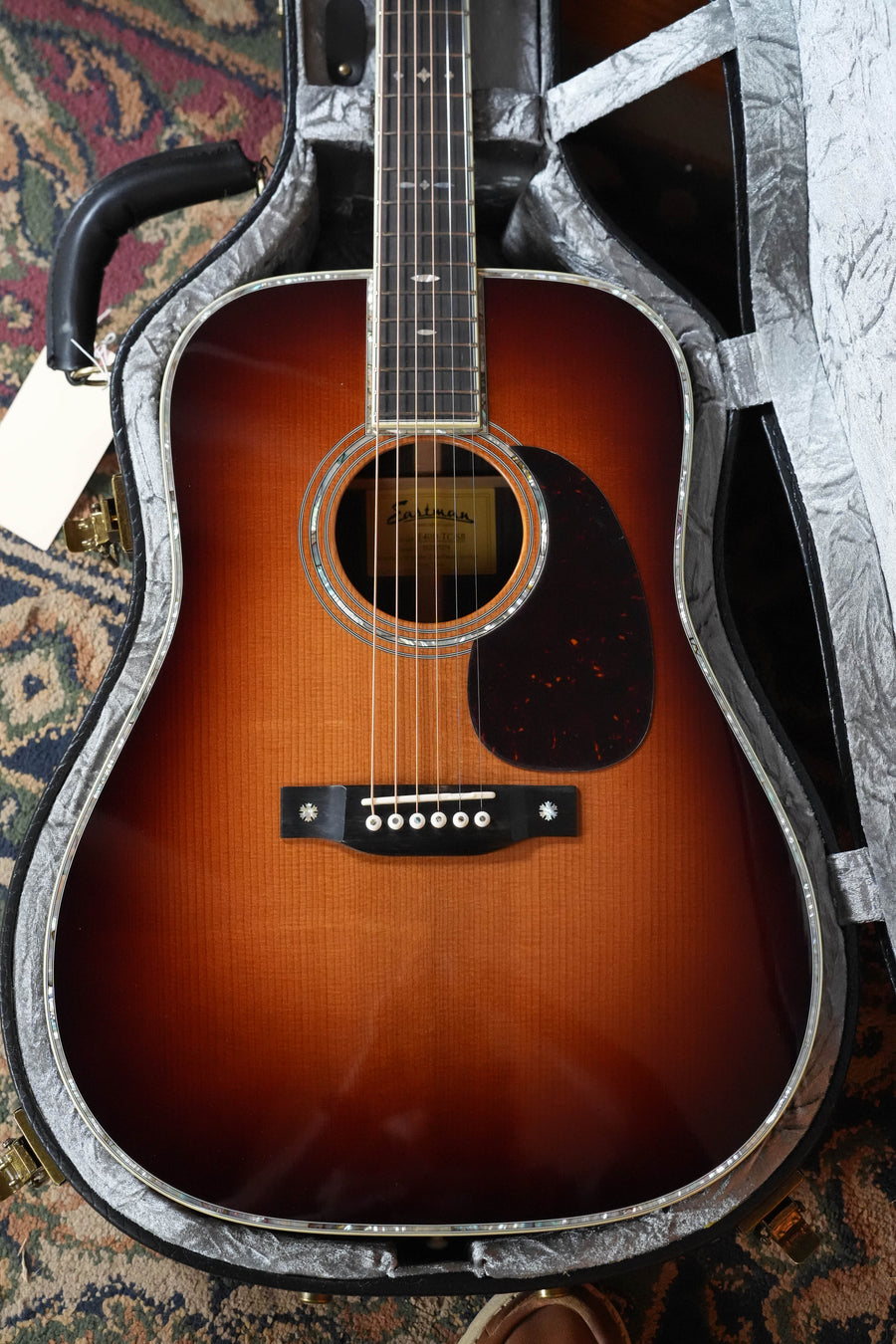 An Eastman Guitars E40D-TC-SB #5274 dreadnought acoustic with a sunburst Thermo-cured AAA Adirondack top, rosewood back/sides, tortoiseshell pickguard, and pearl inlays rests in its hard case on a patterned rug.