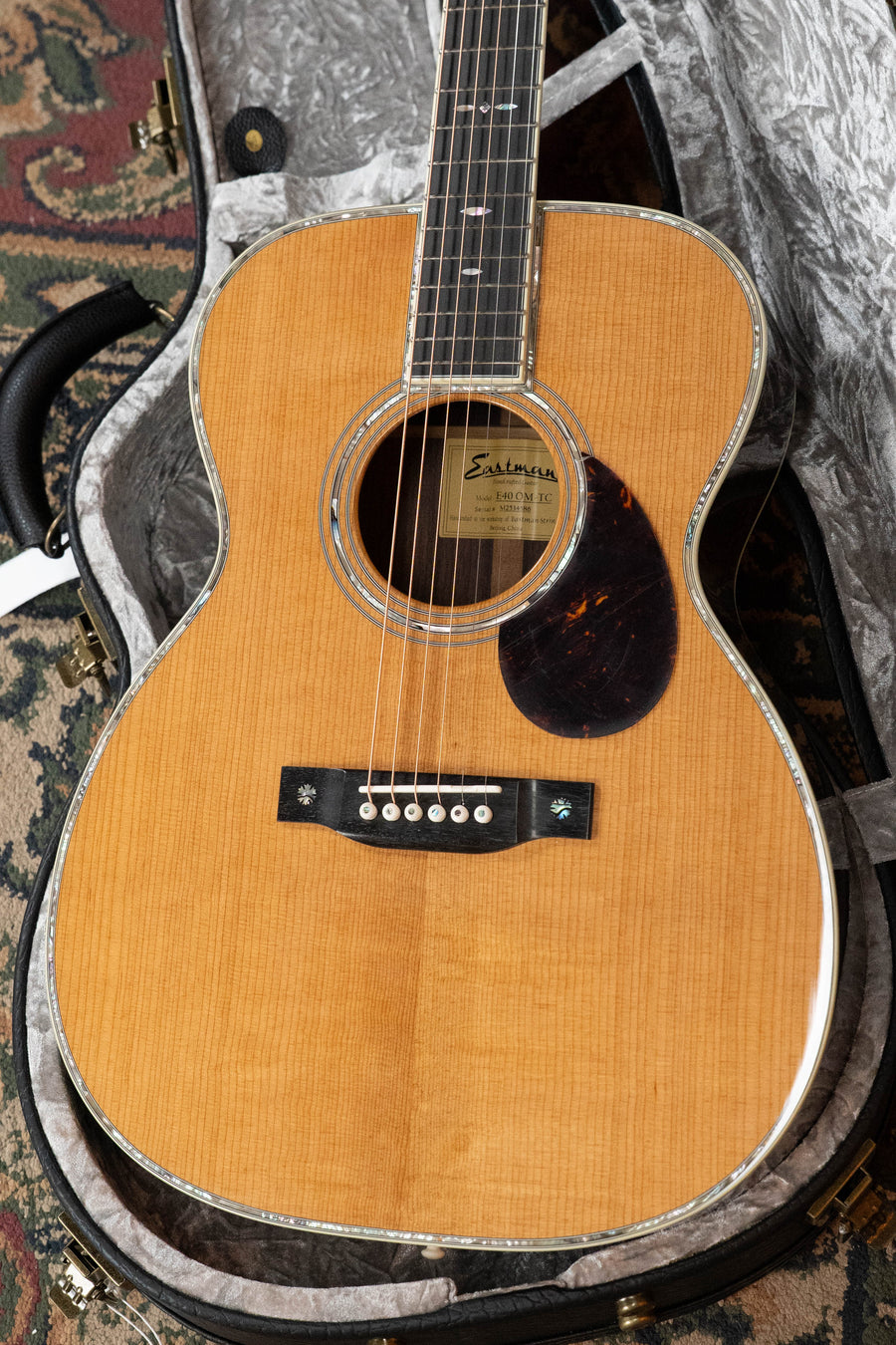 A close-up of the Eastman Guitars E40OM-TC AAA Grade Thermo-cured Adirondack/Rosewood Orchestra Model Acoustic Guitar #4586 with a natural finish, tortoiseshell pickguard, decorative inlays, in a plush gray-lined hard case.