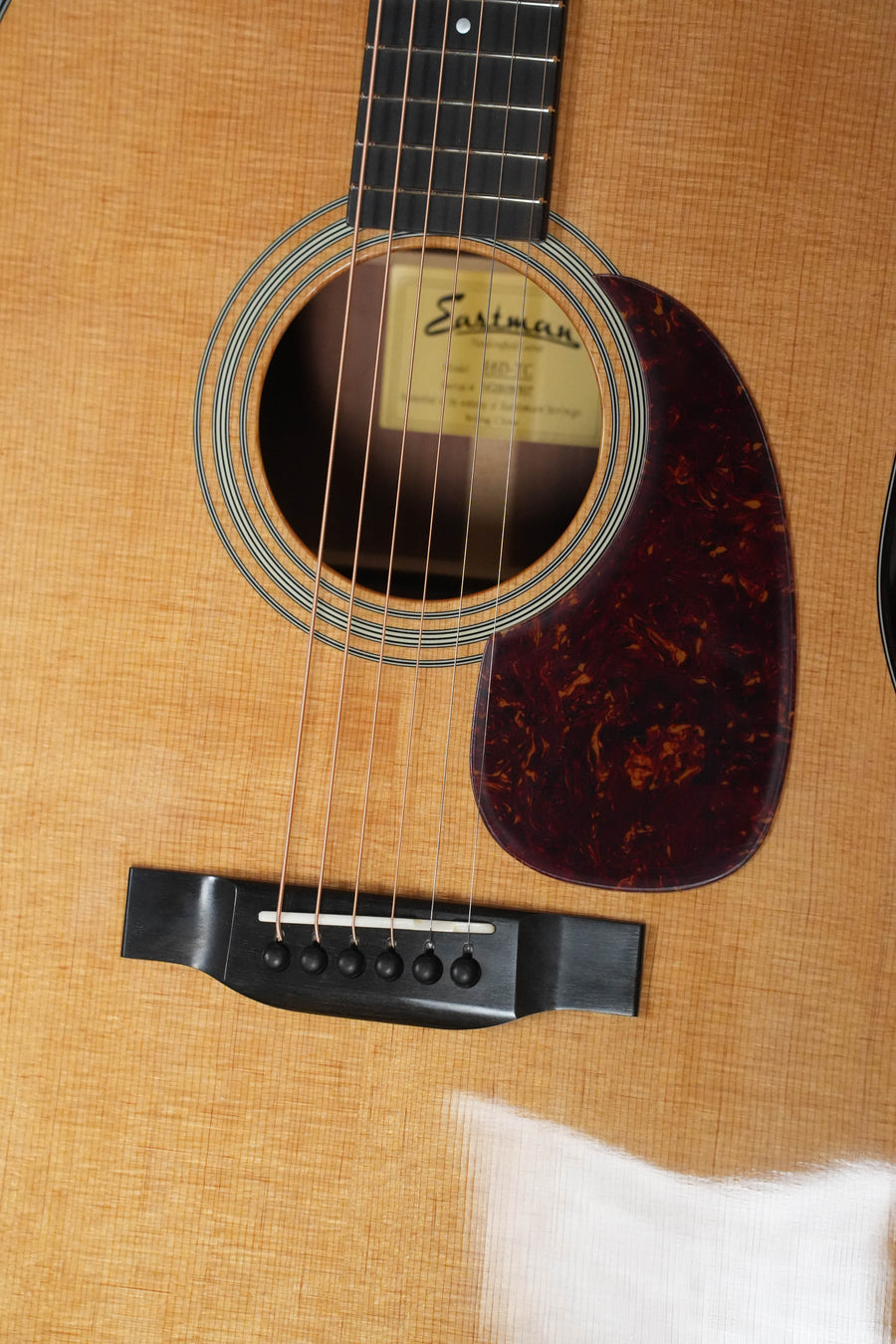 Close-up of the Eastman E6D-TC Dreadnought Acoustic Guitar #8507 by Eastman Guitars, highlighting its strings, sound hole, pickguard, and internal label within a mahogany body and thermo-cured Sitka spruce top grain.