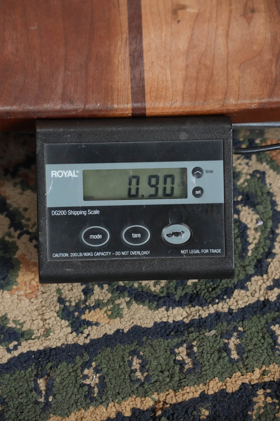 A digital shipping scale on a patterned rug displays 0.90 lbs—ideal for shipping your Eastman EU1-C Sitka/Ovangkol Concert Ukulele #5160 by Eastman Guitars. The ROYAL DG200 Shipping Scale has mode, tare, and power buttons.