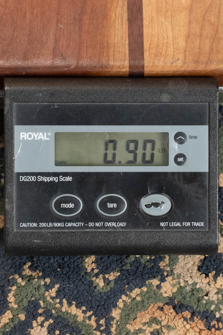 A digital shipping scale on a patterned carpet shows a weight of 0.90 lbs for the Eastman EU3-C All Mahogany Concert Ukulele #8258 by Eastman Guitars, highlighting the instrument’s lightness and easy handling.