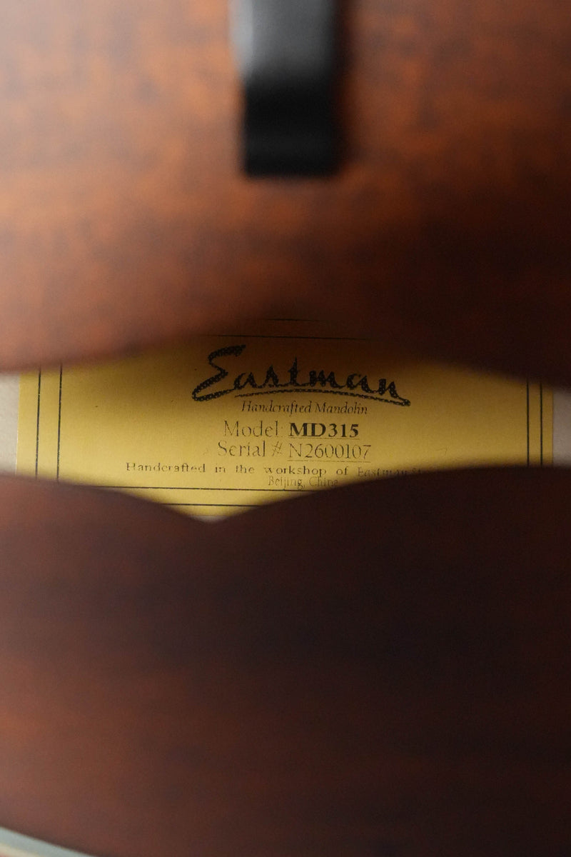 Close-up through the sound hole of an Eastman Guitars MD315 F-Style Hand-Carved Mandolin #0107, showing a label with the model and serial number, crafted for professional tone in Eastman's workshop.
