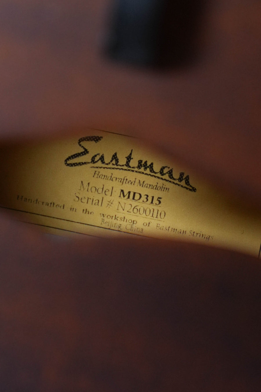 A close-up of the label in an Eastman Guitars MD315 F-Style Hand-Carved Mandolin #0110 shows it was handcrafted in Beijing, China by Eastman Strings.