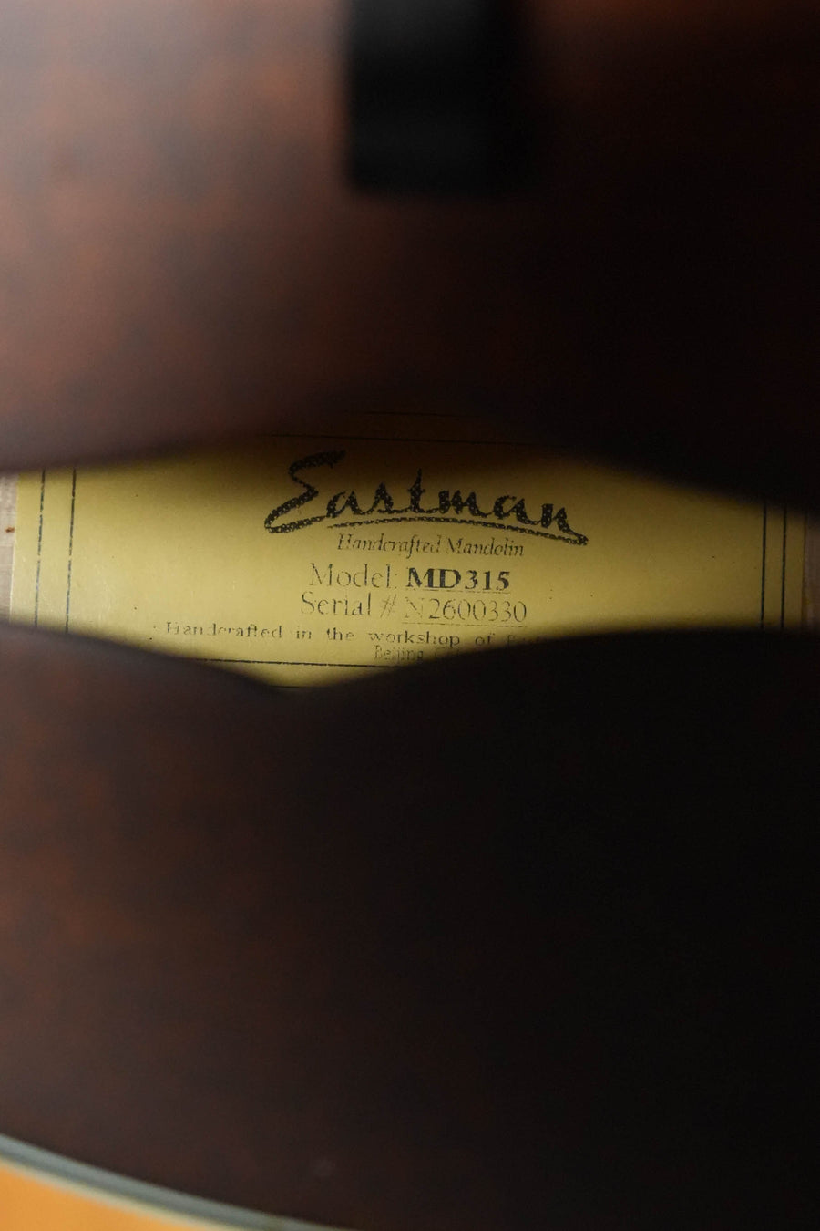 Close-up of the Eastman Guitars MD315 F-Style Hand-Carved Mandolin #0330's interior label, visible through the soundhole, showing model and serial details framed by dark wood and noted for its professional-level tone.