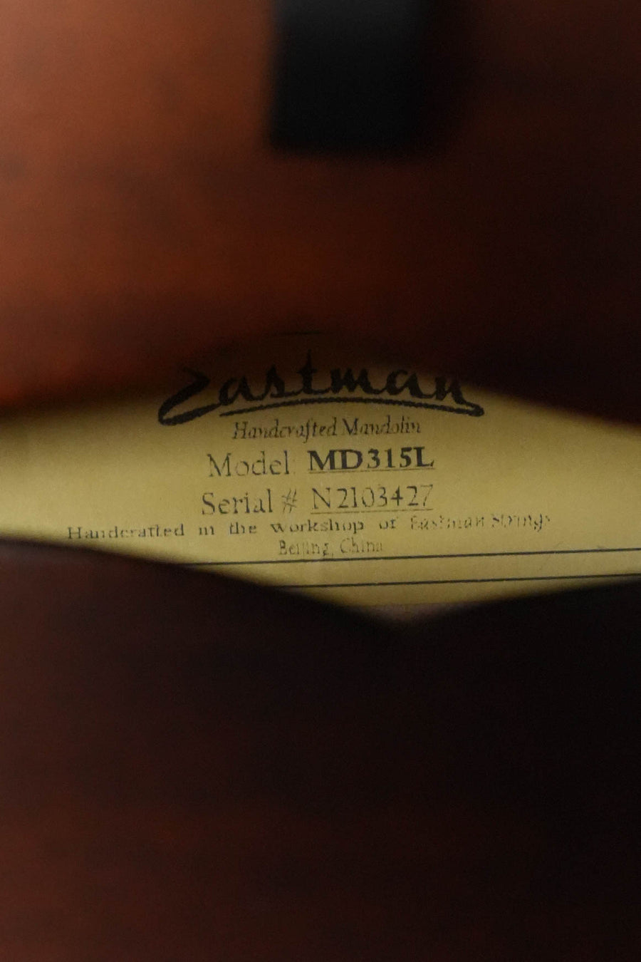 A close-up of the label inside an Eastman Guitars MD315L Left-Handed F-Style Hand-Carved Mandolin #3427, indicating it was crafted from spruce and maple for professional tone in Beijing, China.