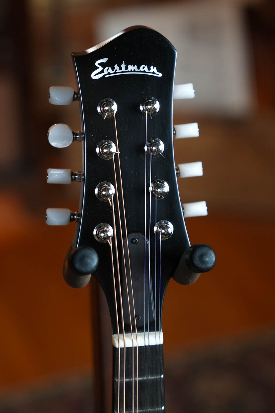 Close-up of the Eastman Guitars MD505CC/TV Comfort Contour True Tone Vintage Series A Style Mandolin #2859 headstock, showing tuning pegs, part of the neck, strings, and the Eastman Guitars logo against a softly blurred background.