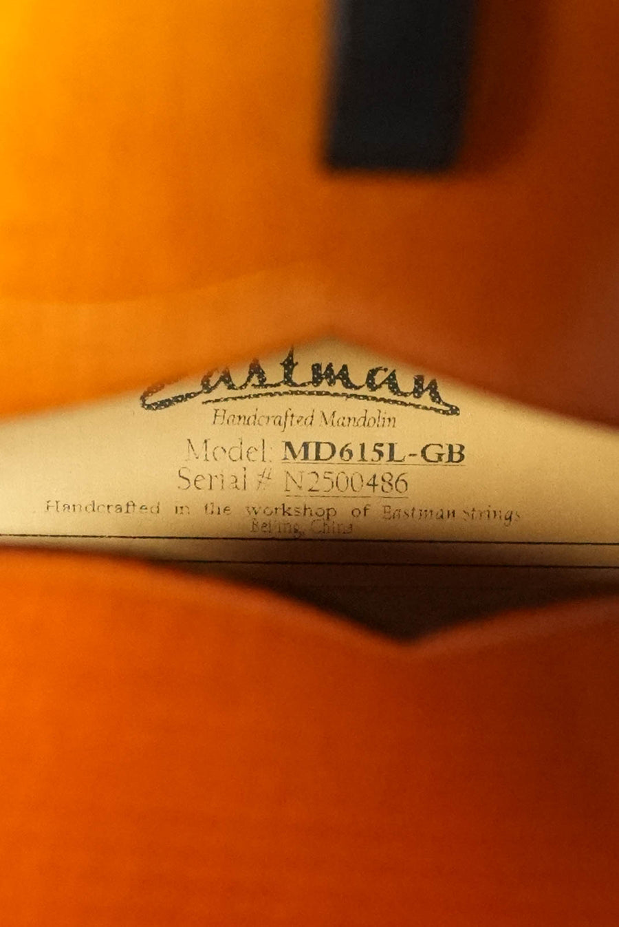 Inside this Eastman Guitars MD615L-GB Goldburst F-Style Mandolin (Left Handed, #0486) is a label attesting to its handcrafted build, K&K pickup, hand-carved tonewoods, and striking orange-brown finish from Beijing.