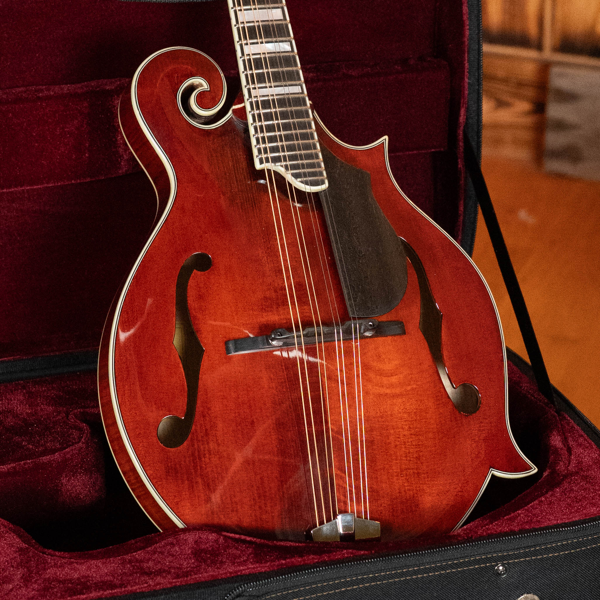 A close-up of the Eastman Guitars MD615 Spruce/Maple F-Style Mandolin w/K&K Pickup (#3918) reveals glossy, hand-carved curves, ornate f-holes, and metal strings, displayed in a velvet-lined black case with rich reddish-brown hues.