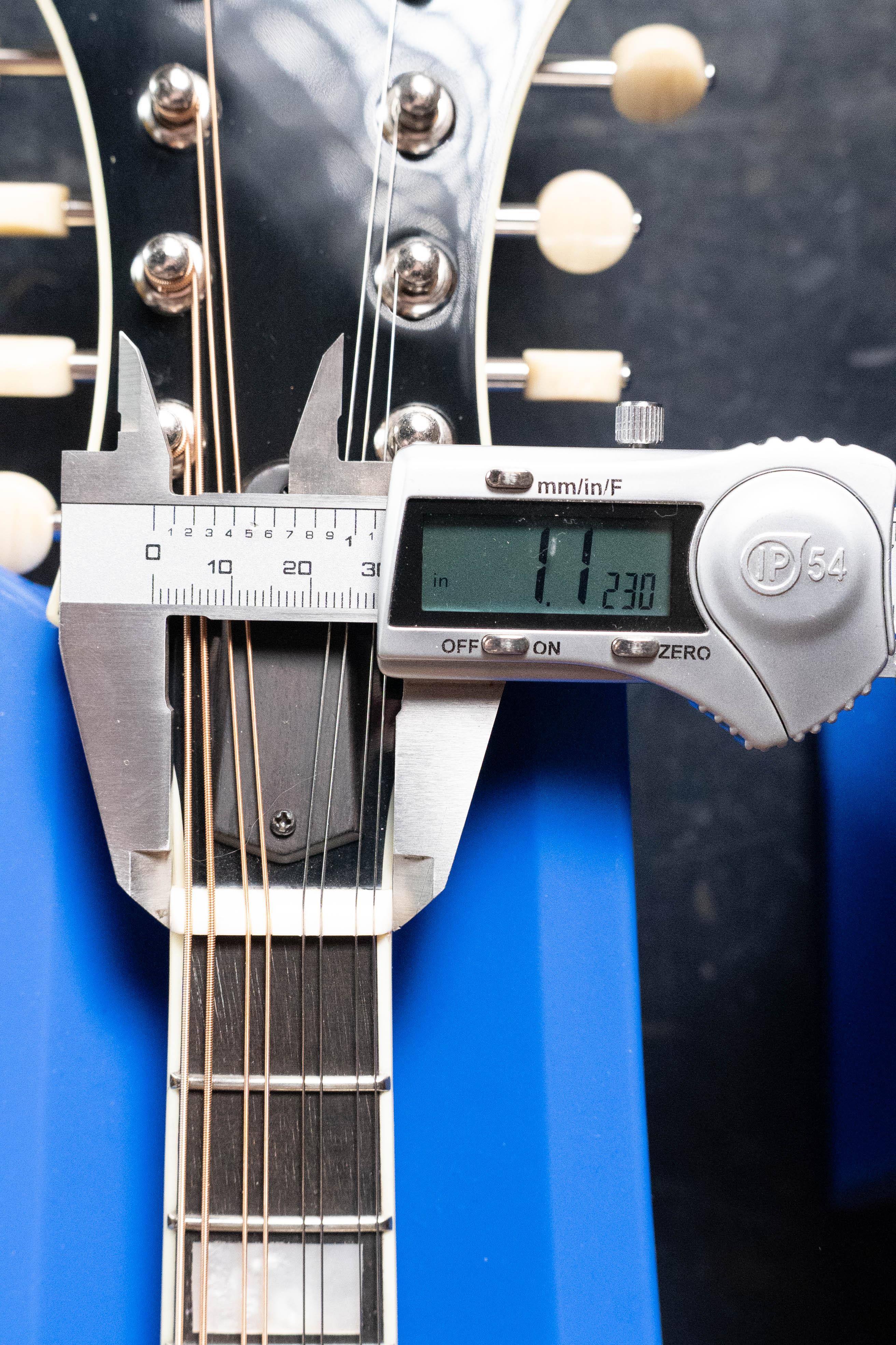A digital caliper measures the Eastman Guitars MD615 Spruce/Maple F-Style Mandolin w/K&K Pickup #3918 neck at the nut, displaying 1.23 inches. This hand-carved mandolin features six strings and ivory-colored tuning pegs.