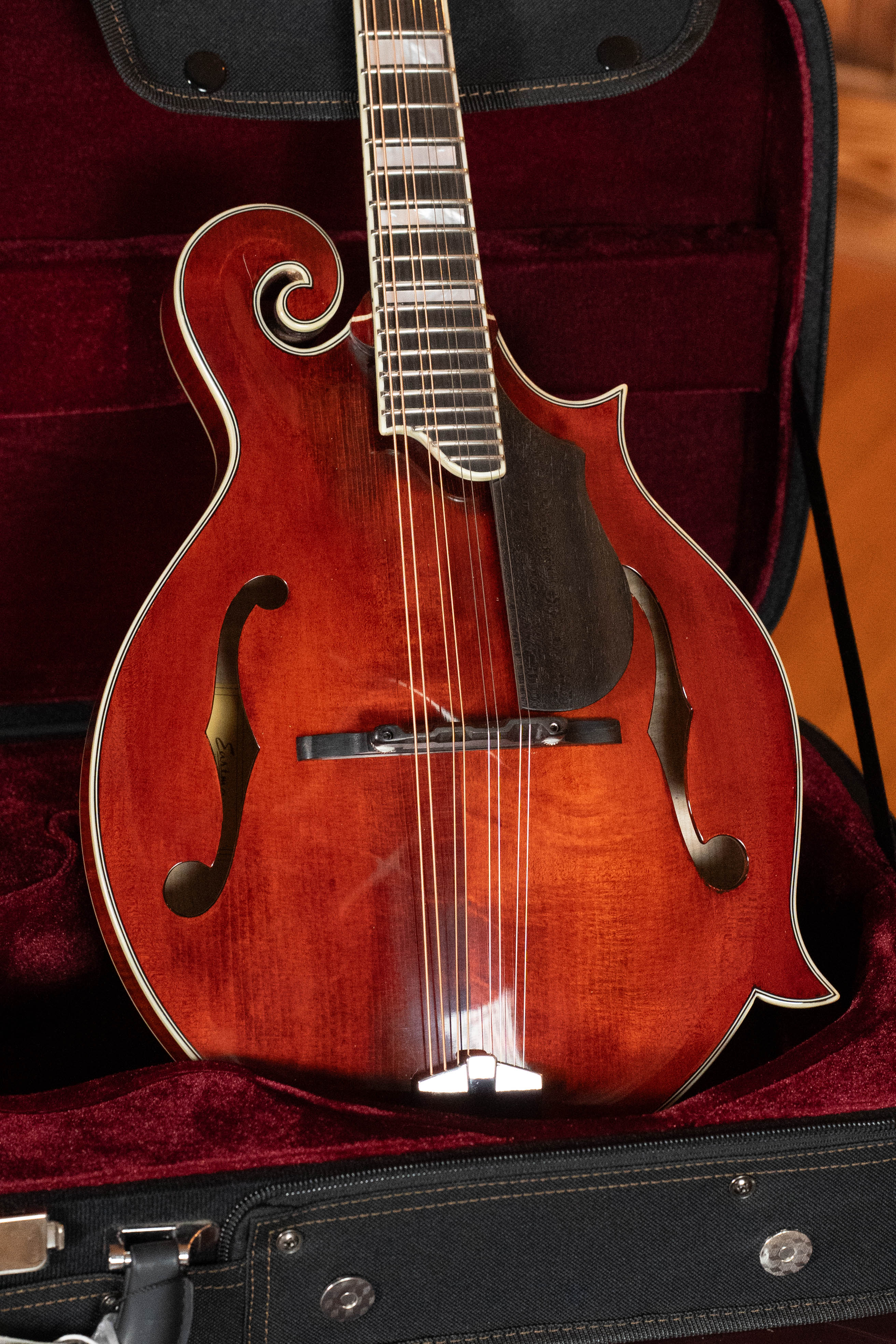 A close-up of an Eastman Guitars MD615 Spruce/Maple F-Style Mandolin w/K&K Pickup #3918, showing its decorative curves and f-holes as it rests in a plush, dark red-lined instrument case.