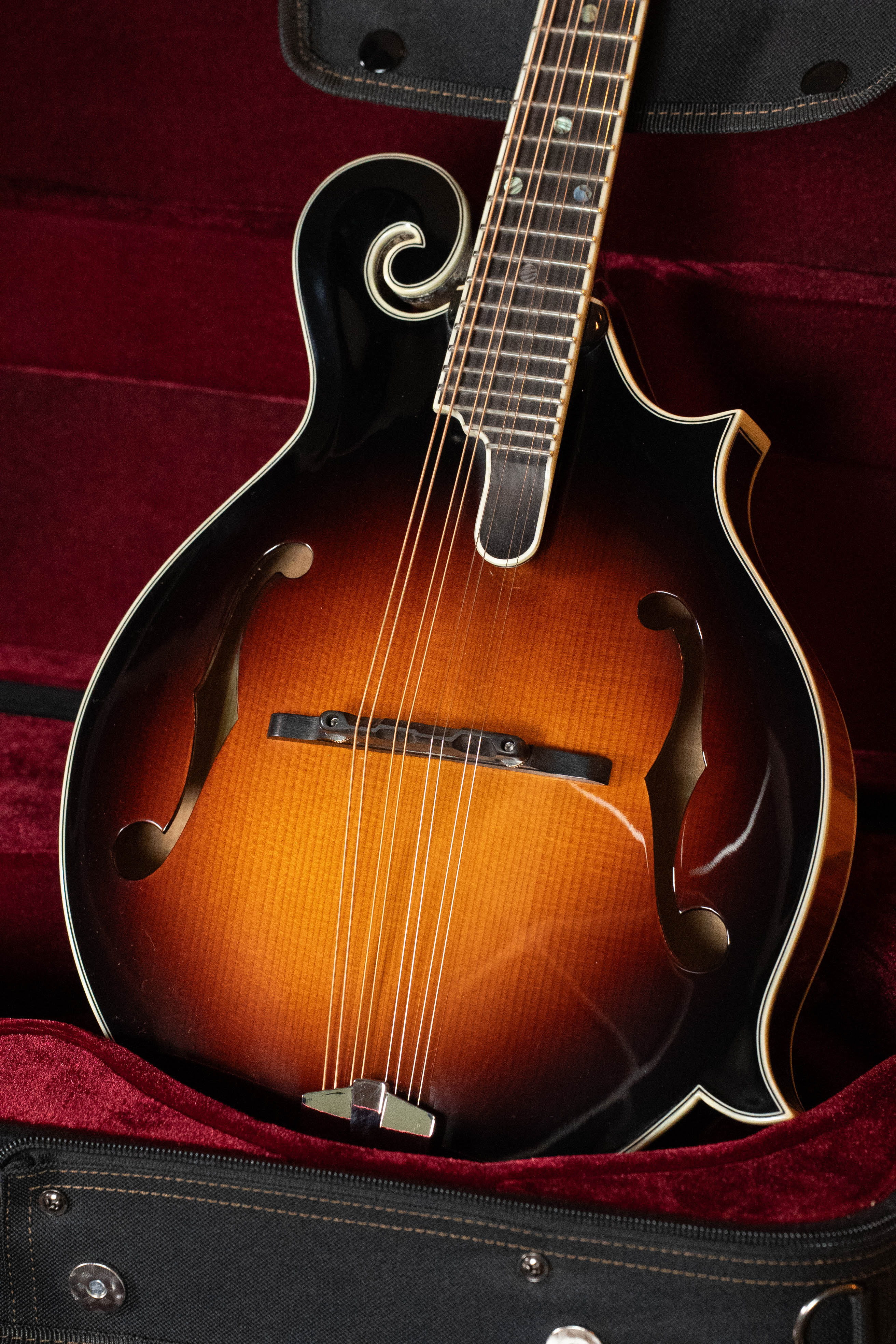 A close-up of the Eastman Guitars MD815-SB Adirondack/Flamed Maple Sunburst F-Style Mandolin #3355, highlighting its elegant curves and sunburst finish, resting in a plush red-lined case.