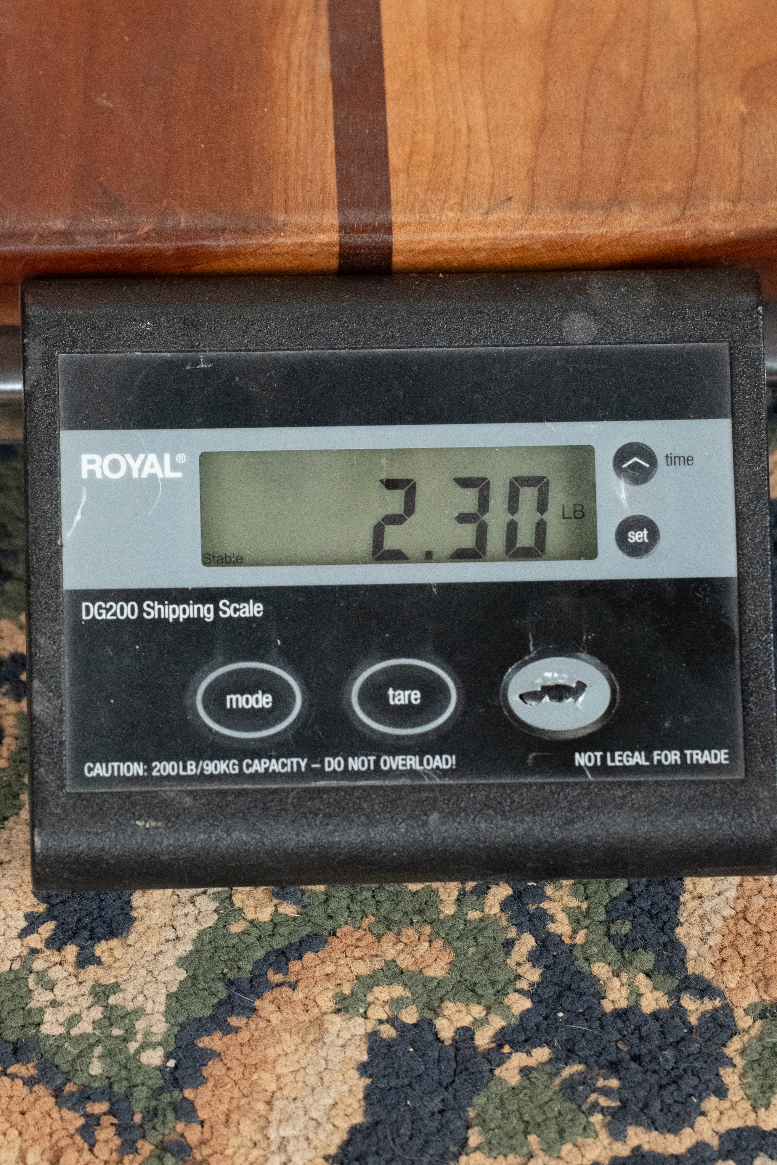 A digital shipping scale shows 2.30 lbs while supporting part of an Eastman Guitars MD815-SB Adirondack/Flamed Maple Sunburst F-Style Mandolin #3355, its finish resting on the black device atop patterned carpet.
