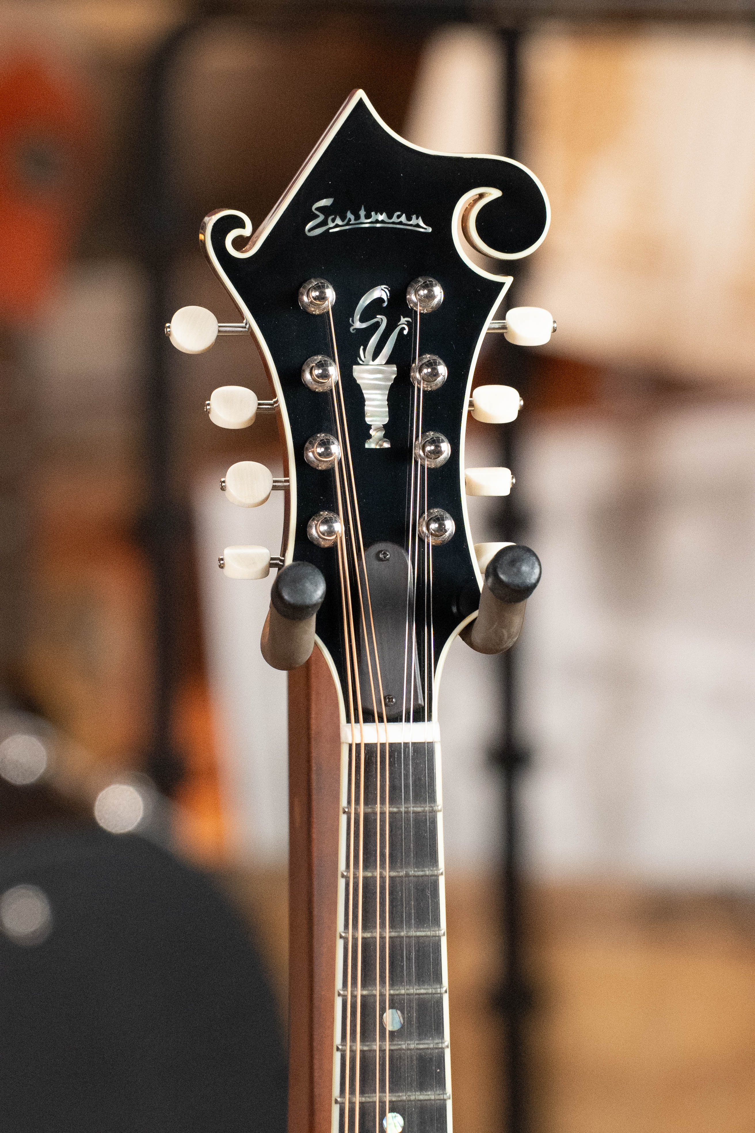 Close-up of the Eastman Guitars MD815-SB Adirondack/Flamed Maple Sunburst F-Style Mandolin #3355 headstock, featuring white tuning pegs, detailed inlay, and the "Eastman" logo, showcasing fine craftsmanship against a blurred background.