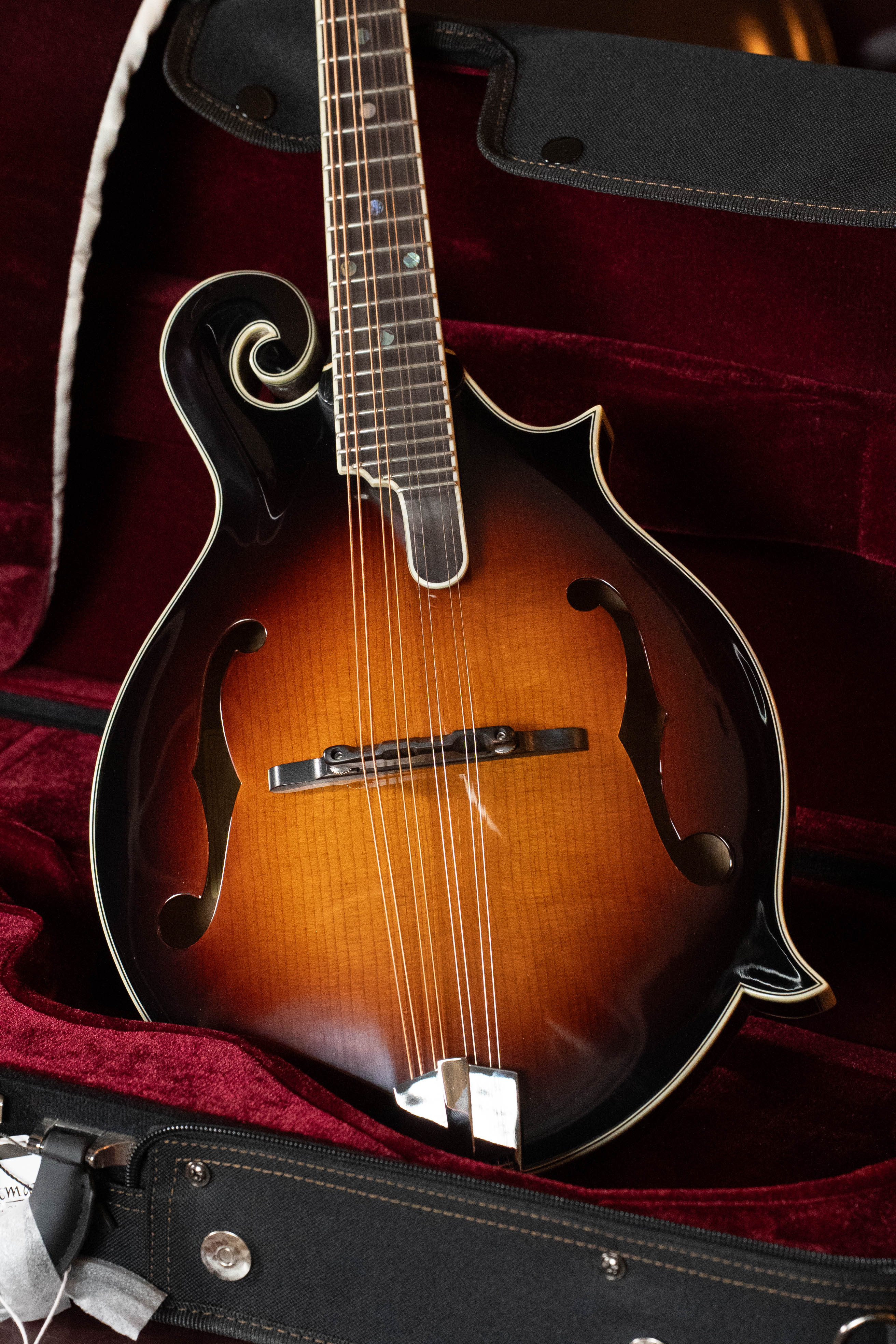 An Eastman Guitars MD815-SB Adirondack/Flamed Maple Sunburst F-Style Mandolin #3356 with elegant curves and f-holes rests in a plush, red velvet-lined hard case.