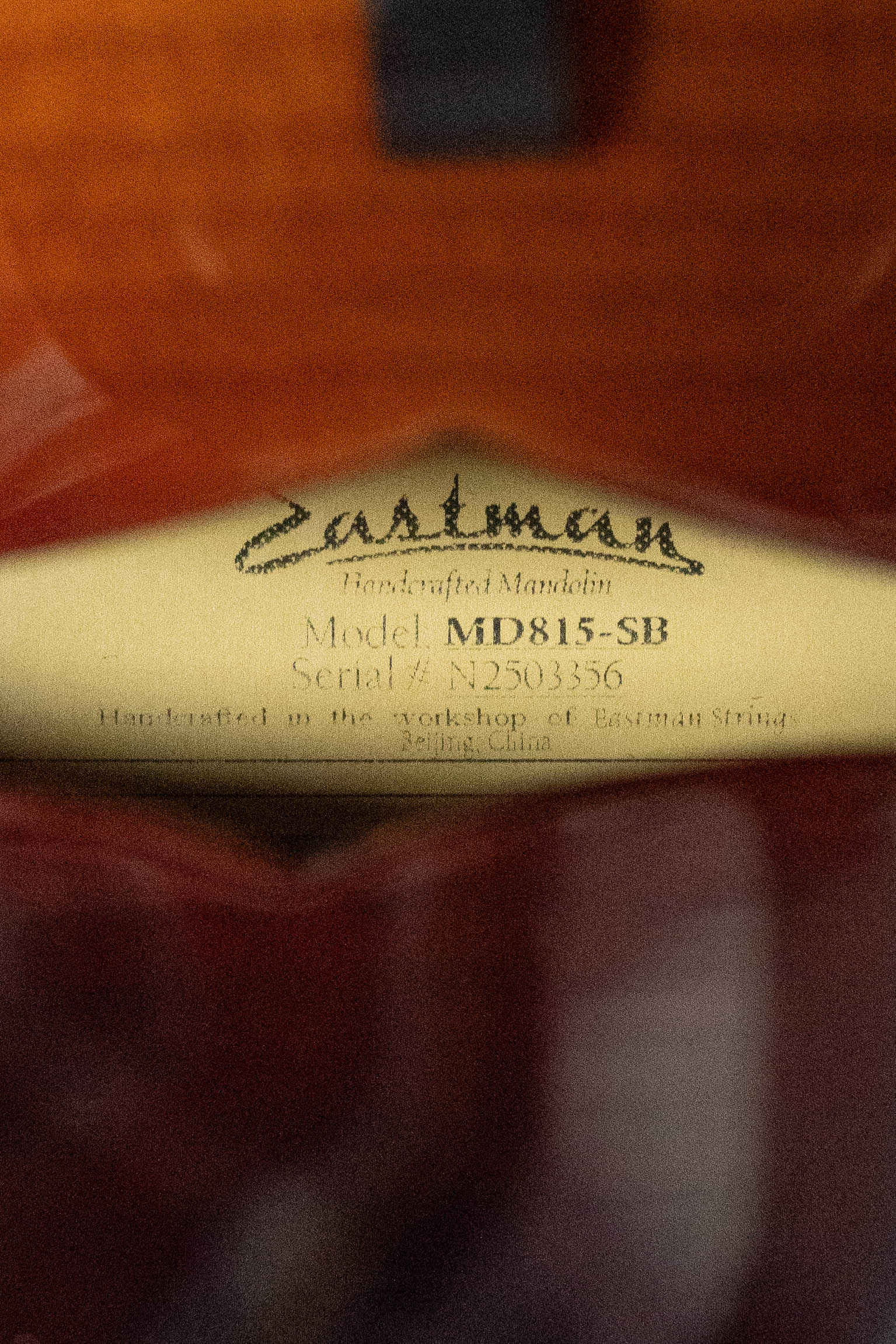 Close-up of a label inside an Eastman Guitars MD815-SB Adirondack/Flamed Maple Sunburst F-Style Mandolin #3356, reading: Handcrafted Mandolin, Model MD815-SB, Serial #: N2503356, made in Beijing, China.