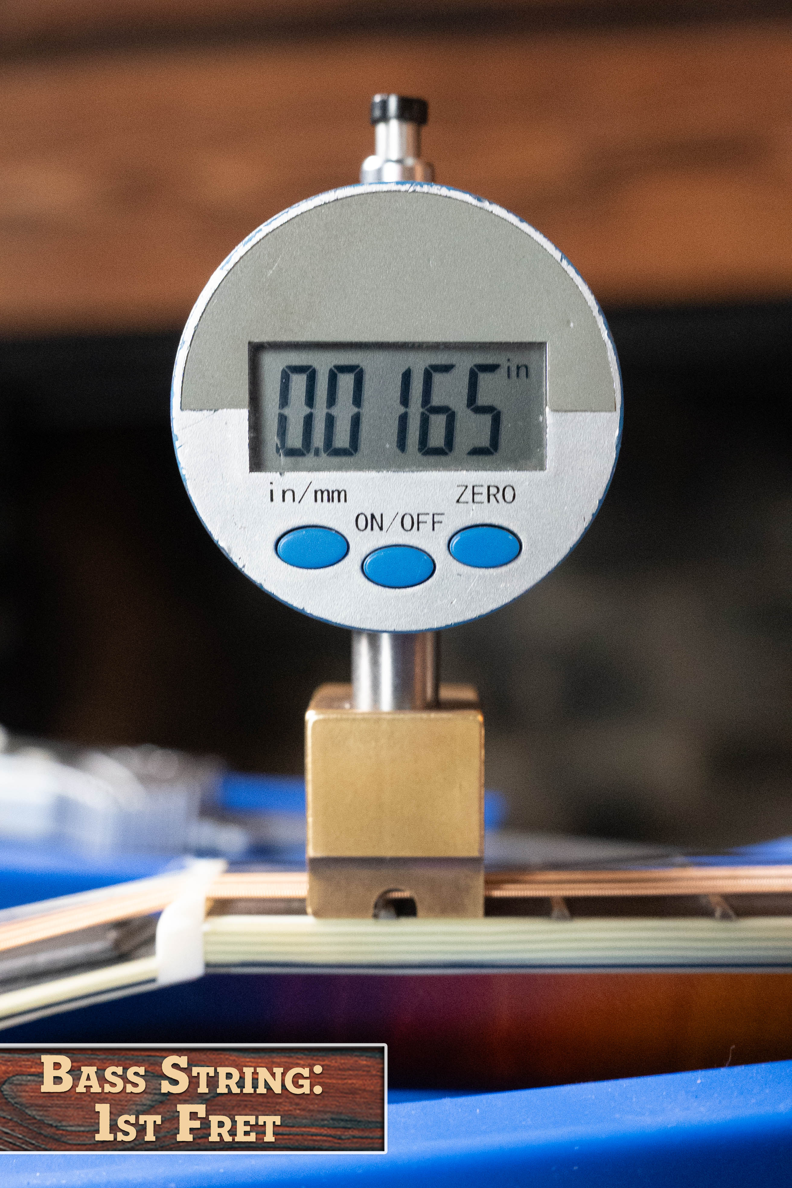 A digital gauge reads 0.0165 inches, showing the string height at the 1st fret—next to an Eastman Guitars MD815-SB Adirondack/Flamed Maple Sunburst F-Style Mandolin #3356. A sign in front says, Bass String: 1st Fret.