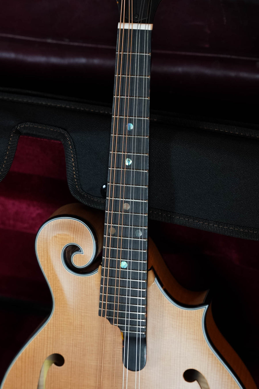 Close-up of an Eastman Strings MD915-BD F-style mandolin (#5821), showing its strings, frets, dot inlays, and ornate scroll on the Adirondack spruce top. The mandolin rests in a cushioned, dark-lined case.