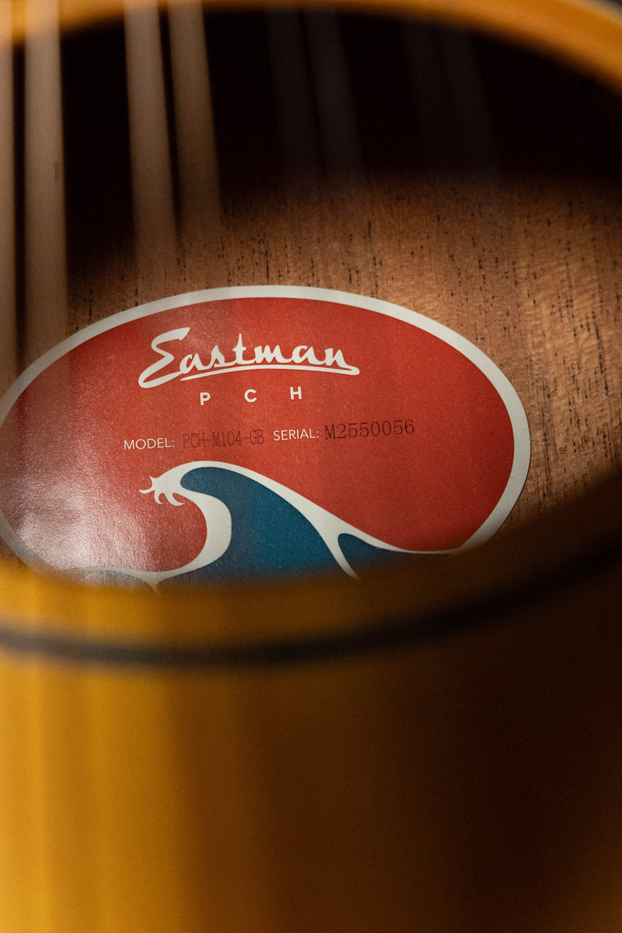 Close-up of a guitar’s sound hole showing a red and blue Eastman Guitars PCH label, with model and serial number partly hidden—like inside the Eastman PCH-M104-GB Goldburst A-Style Mandolin #0056, Solid Spruce/Mahogany.