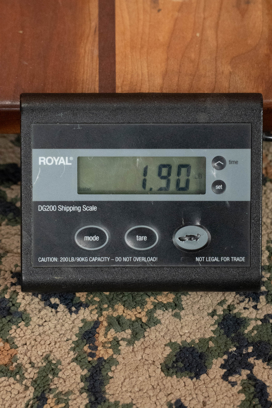 A digital shipping scale reads 1.90 pounds as the Eastman Guitars PCH-M104-GB Solid Spruce/Laminated Mahogany Goldburst Flattop A-Style Mandolin #0056 sits beside a wooden surface on patterned carpet.
