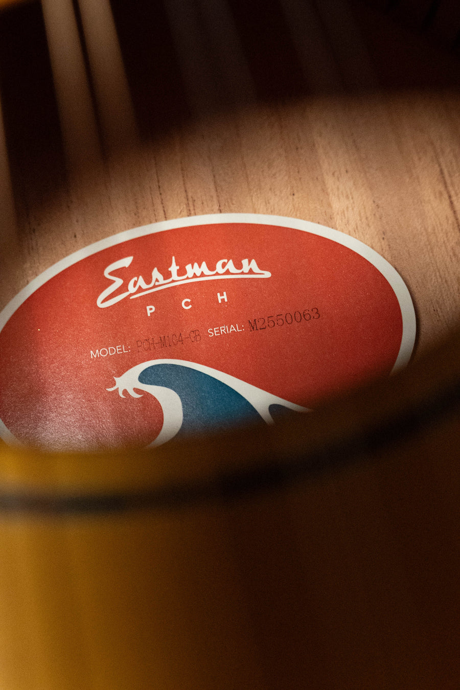 Close-up of an Eastman Guitars label inside a PCH-M104-GB Solid Spruce/Laminated Mahogany Goldburst A-Style Mandolin #0063, showing wood grain and the yellow finish details.