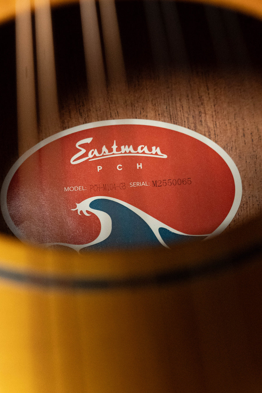 Close-up of a mandolin's soundhole with an inside label showing Eastman Guitars PCH-M104-GB Solid Spruce/Laminated Mahogany Goldburst Flattop A-Style Mandolin #0065—ideal for fans or beginners seeking quality craftsmanship.