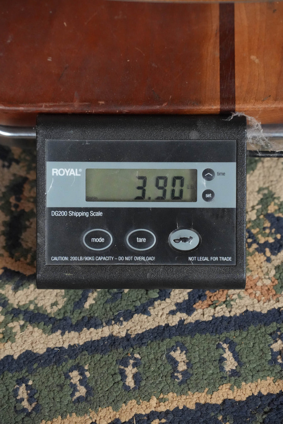 A digital shipping scale on a patterned carpet shows 3.90 lbs as it supports part of an Eastman Guitars PCH1-D Solid Sitka/Laminated Sapele Dreadnought Acoustic Guitar #1819.