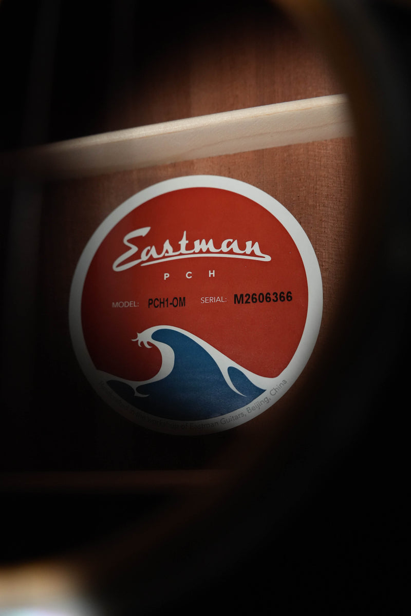 Close-up of the Eastman Guitars PCH1-OM Orchestra Model Acoustic Guitar #6366 label inside the sound hole, showing a red and blue wave logo and Truetone Satin finish.