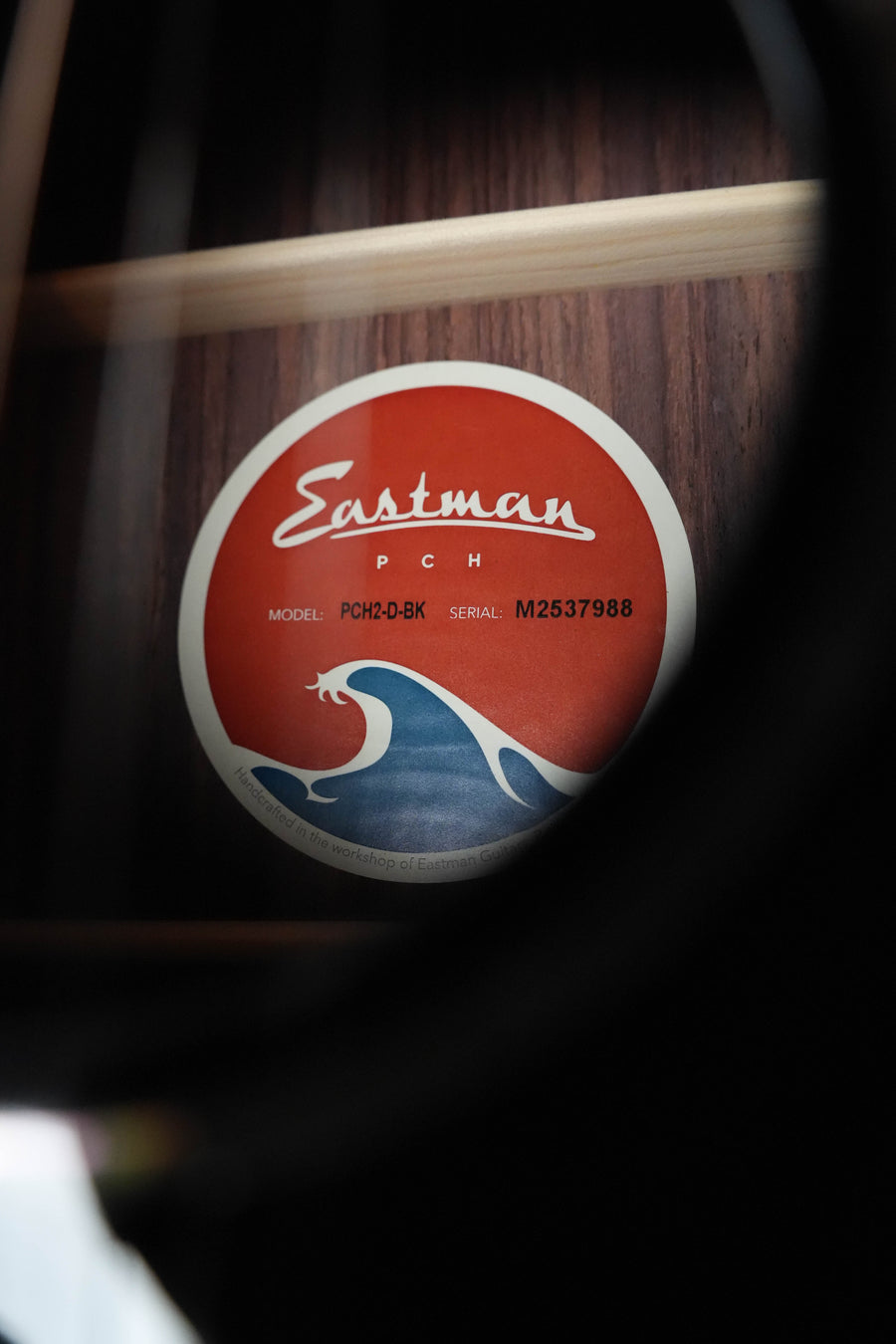 A close-up through the sound hole reveals the Eastman Guitars PCH label inside a dreadnought, showing model PCH2-D-BK with its solid Sitka spruce top and laminated rosewood back and sides, finished in black.