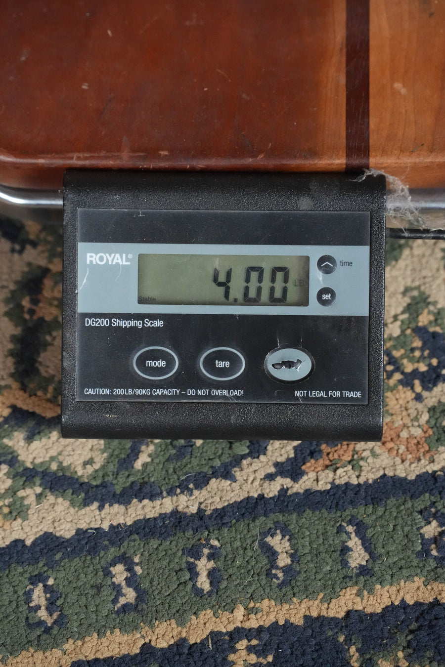 A digital shipping scale on a patterned carpet, partially under wood, shows 4.00 pounds as it weighs an Eastman Guitars PCH2-D-BK Solid Sitka/Laminated Rosewood Black Top Dreadnought Acoustic Guitar #7988.