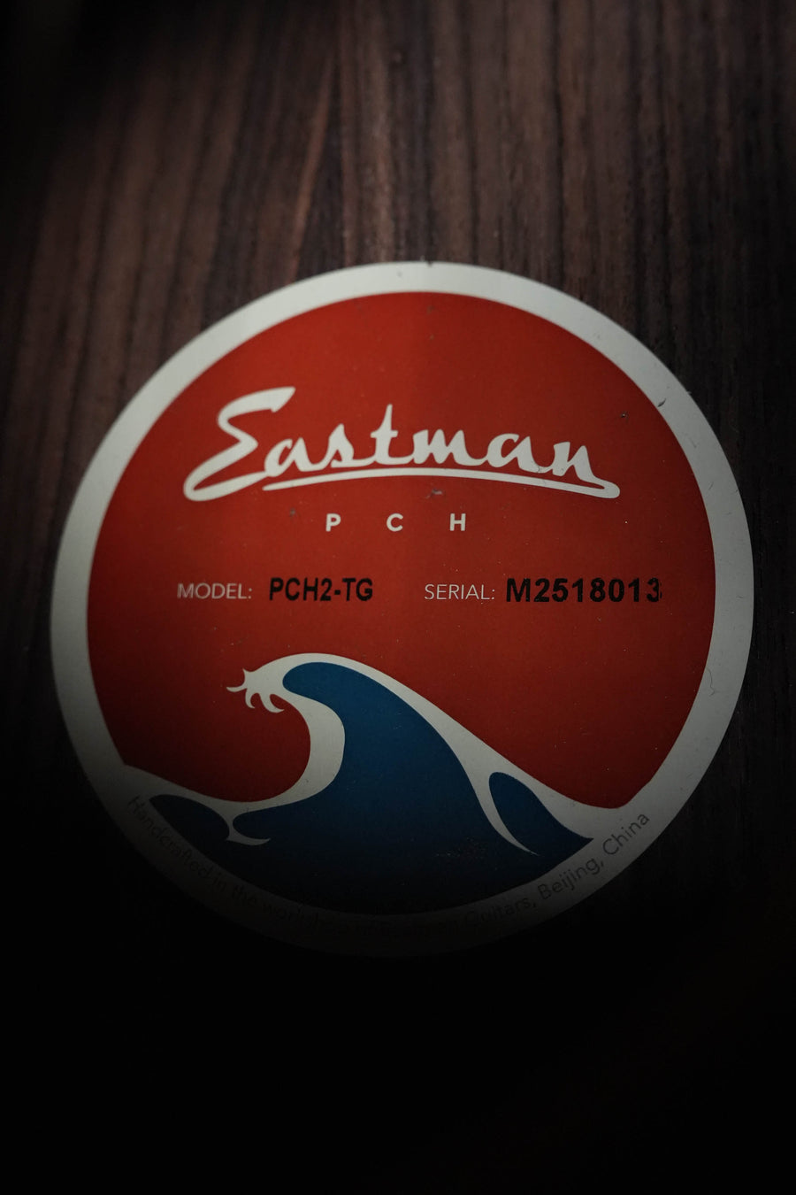 A red and white circular Eastman Guitars label with a wave design appears on the PCH2-TG Thermo-Cured Solid Sitka/Laminated Rosewood Travel Acoustic Guitar #8013, set against a dark wood surface.
