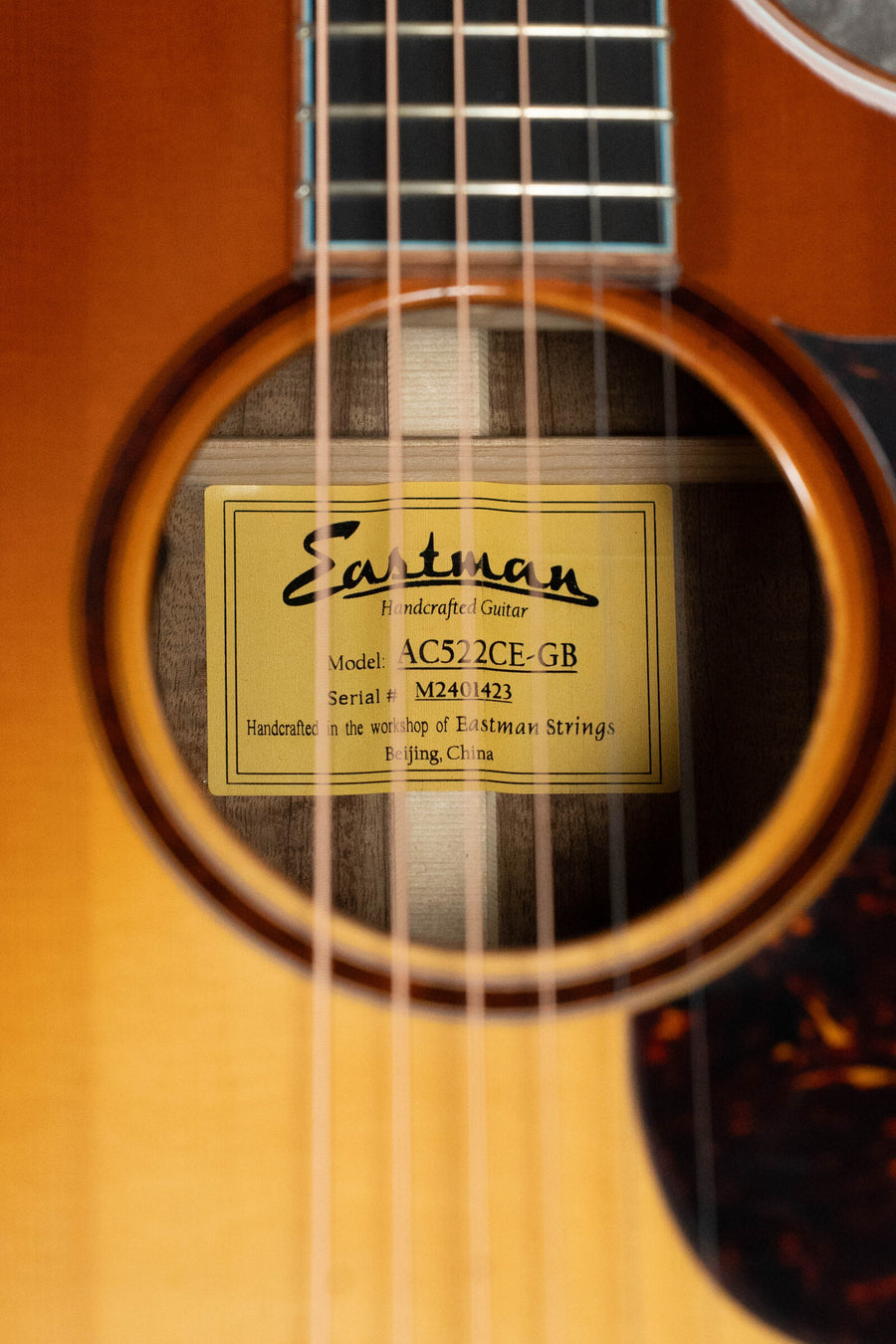 Close-up of the *Dread-Not Certified Used* Eastman AC522CE-GB Goldburst Grand Auditorium by Eastman Guitars, showing its soundhole, yellow label, solid mahogany features, and LR Baggs pickup for superb sound. Model #1423.