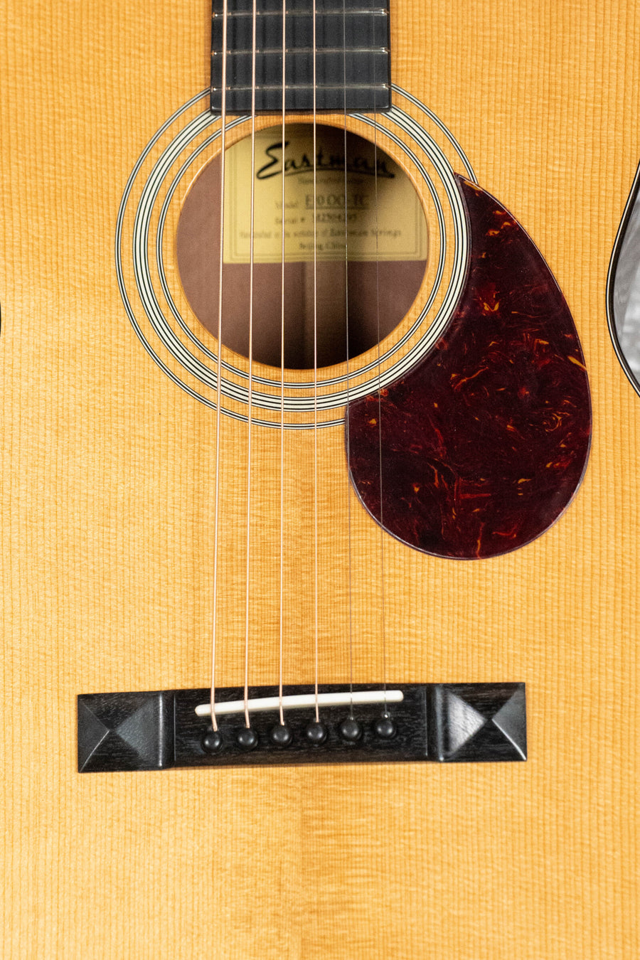 Close-up of the Eastman Guitars E10OO-TC Thermo-Cure Adirondack/Mahogany Acoustic Guitar #4295, highlighting its strings, bridge, sound hole label, and tortoiseshell pickguard on a vintage-style Thermo-Cured Adirondack Spruce top.