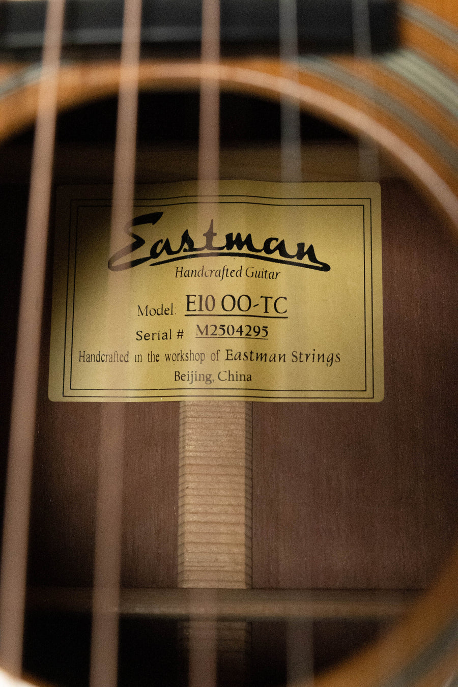 Close-up of the Eastman Guitars E10OO-TC Thermo-Cure Adirondack/Mahogany Acoustic Guitar #4295 label inside the soundhole highlights its handcrafted quality and vintage Pre-War parlor style, framed by visible guitar strings.