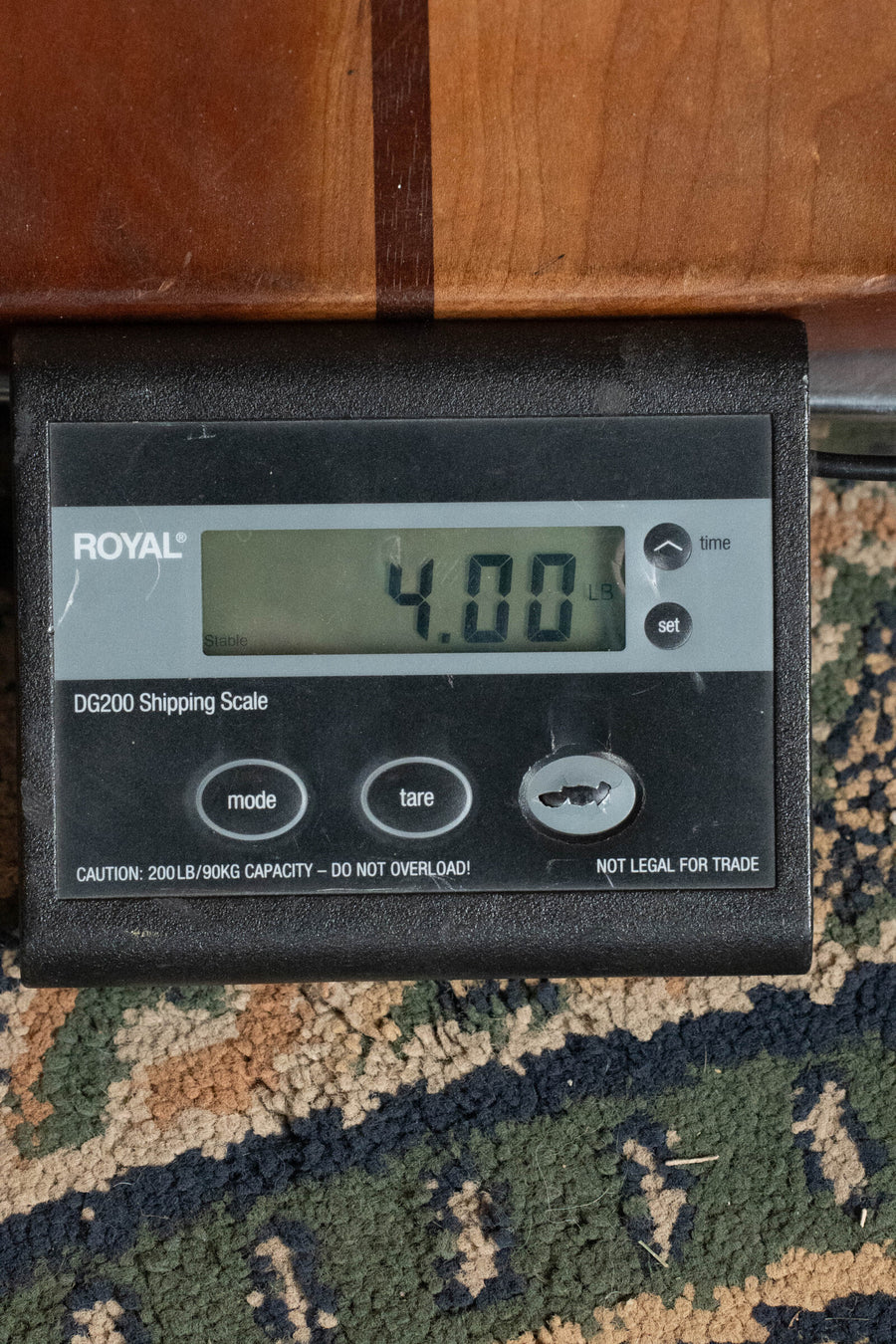 A digital shipping scale shows 4.00 pounds, with part of the Eastman Guitars E10OO-TC Thermo-Cure Adirondack/Mahogany Acoustic Guitar #4295 visible above the display on a patterned carpet.