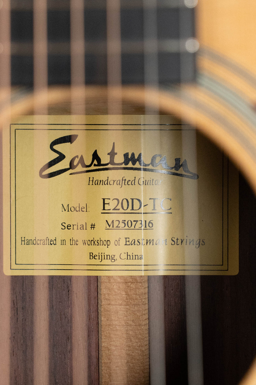 Close-up of Eastman E20D-TC guitar label inside the body with wood grain and strings visible. - Eastman E20D-TC Thermo-Cured Adirondack/Rosewood Dreadnought Acoustic Guitar #7316 - Default Title